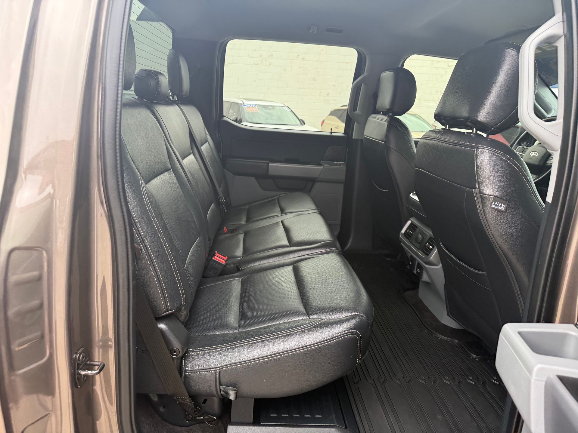 Black leather truck interior, back seats. Tan door frame, gray center console.
