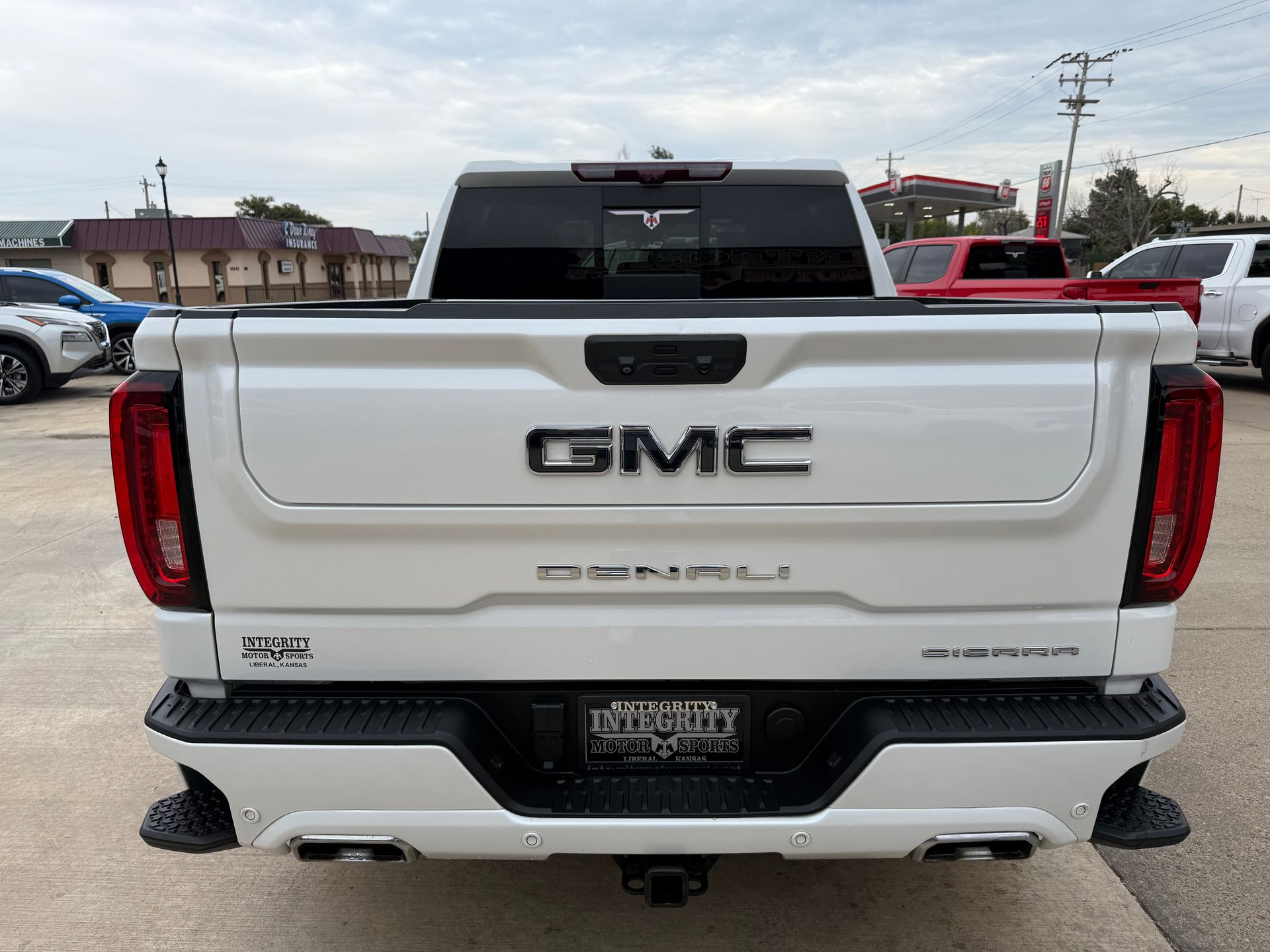 White GMC Denali pickup truck rear view, black accents, overcast sky.