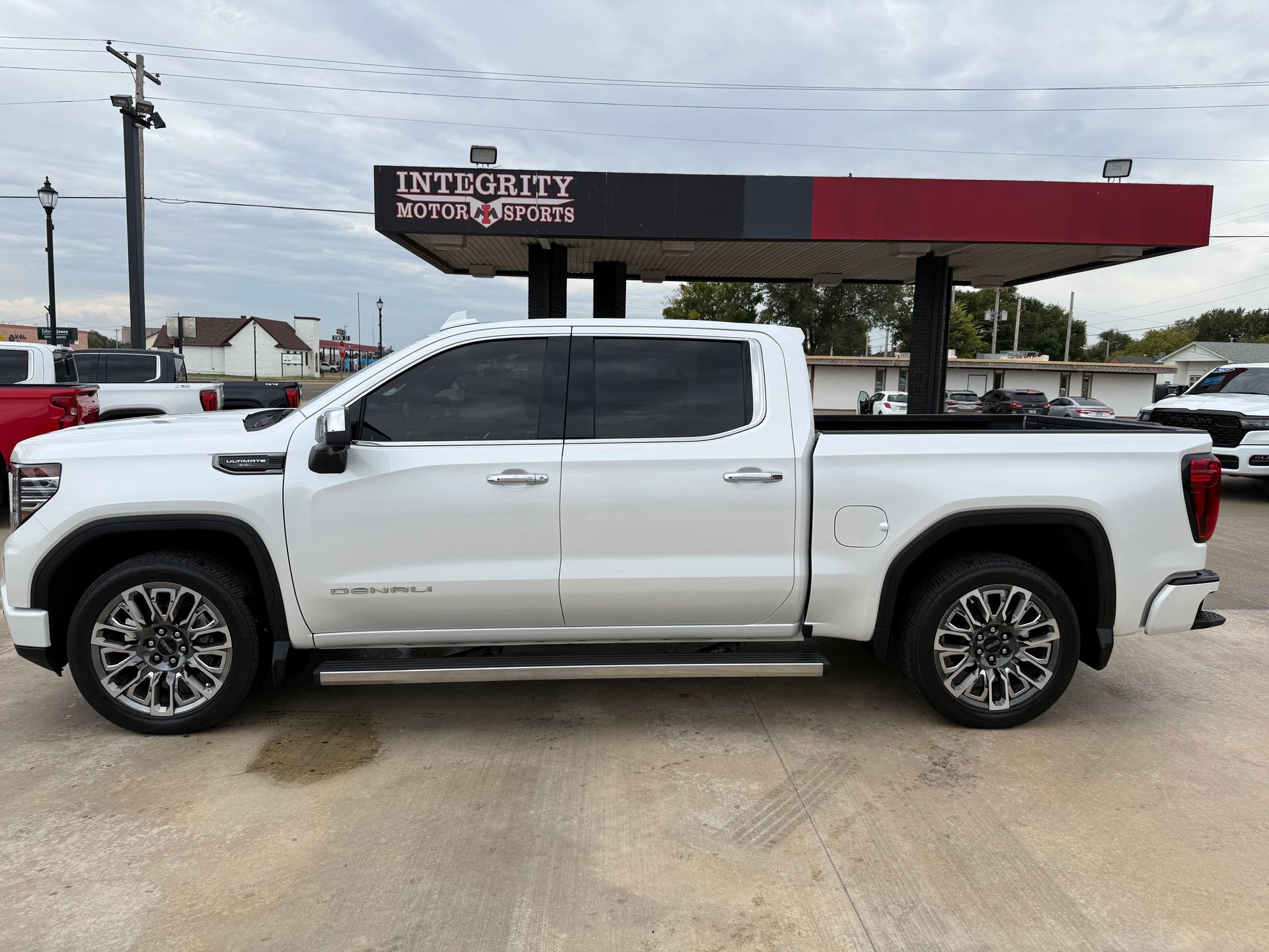 White GMC Sierra Denali pickup truck parked under a red and black canopy, at a dealership.