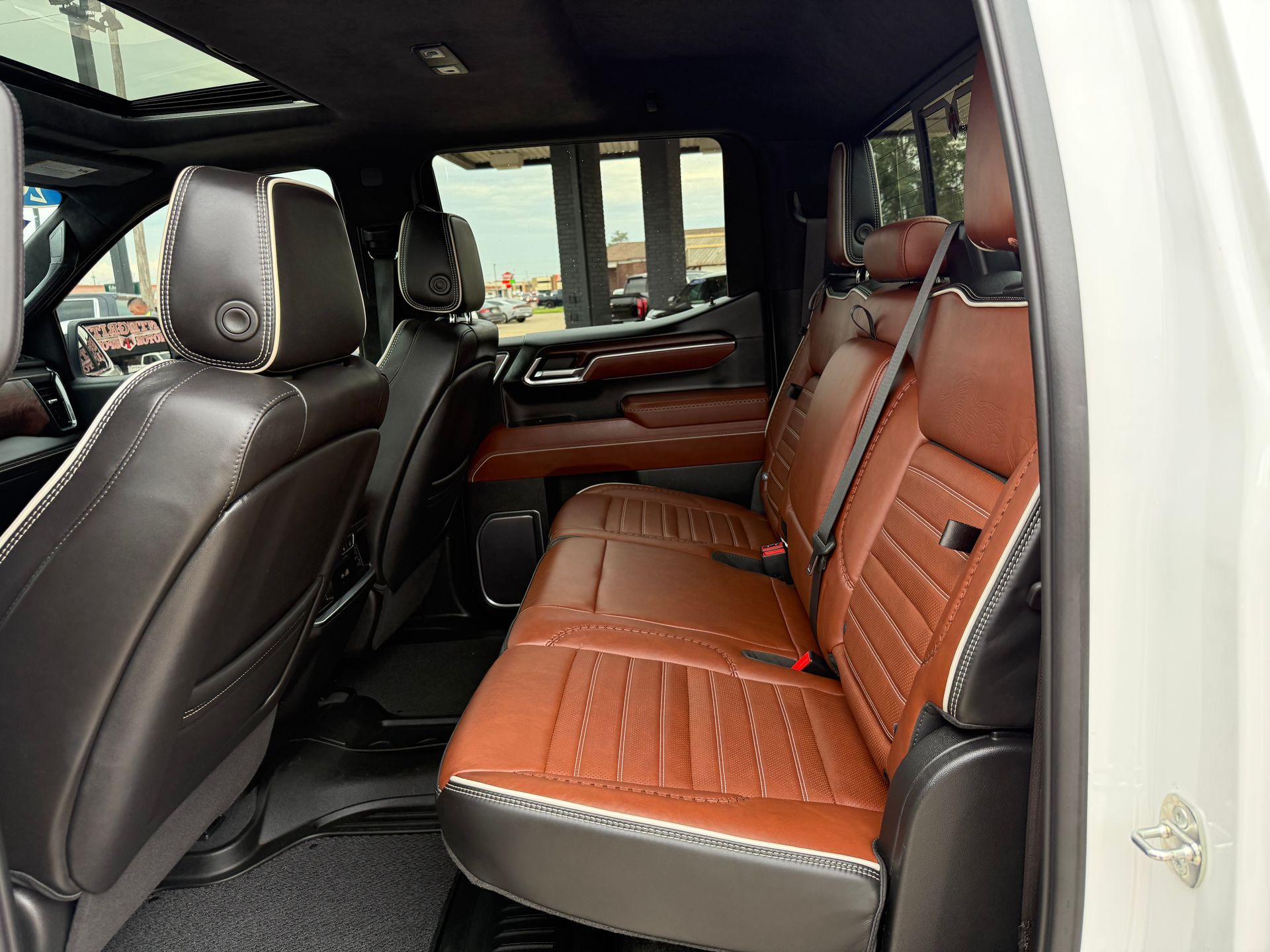 Inside a white truck: brown and black leather seats, sunroof, and open door.