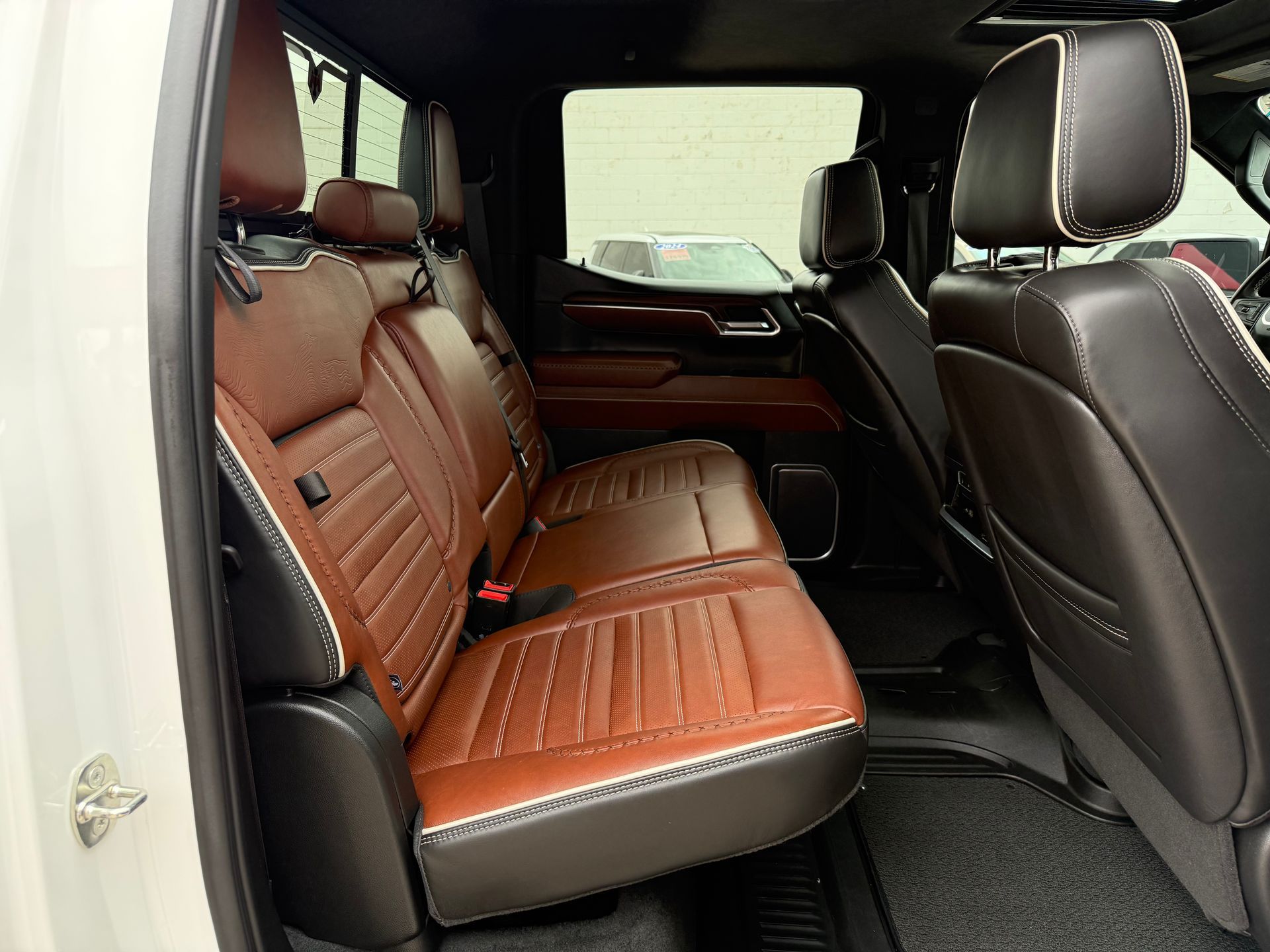 Brown and black leather truck back seat.  White trim, stitched design. Black door and floor mats visible.