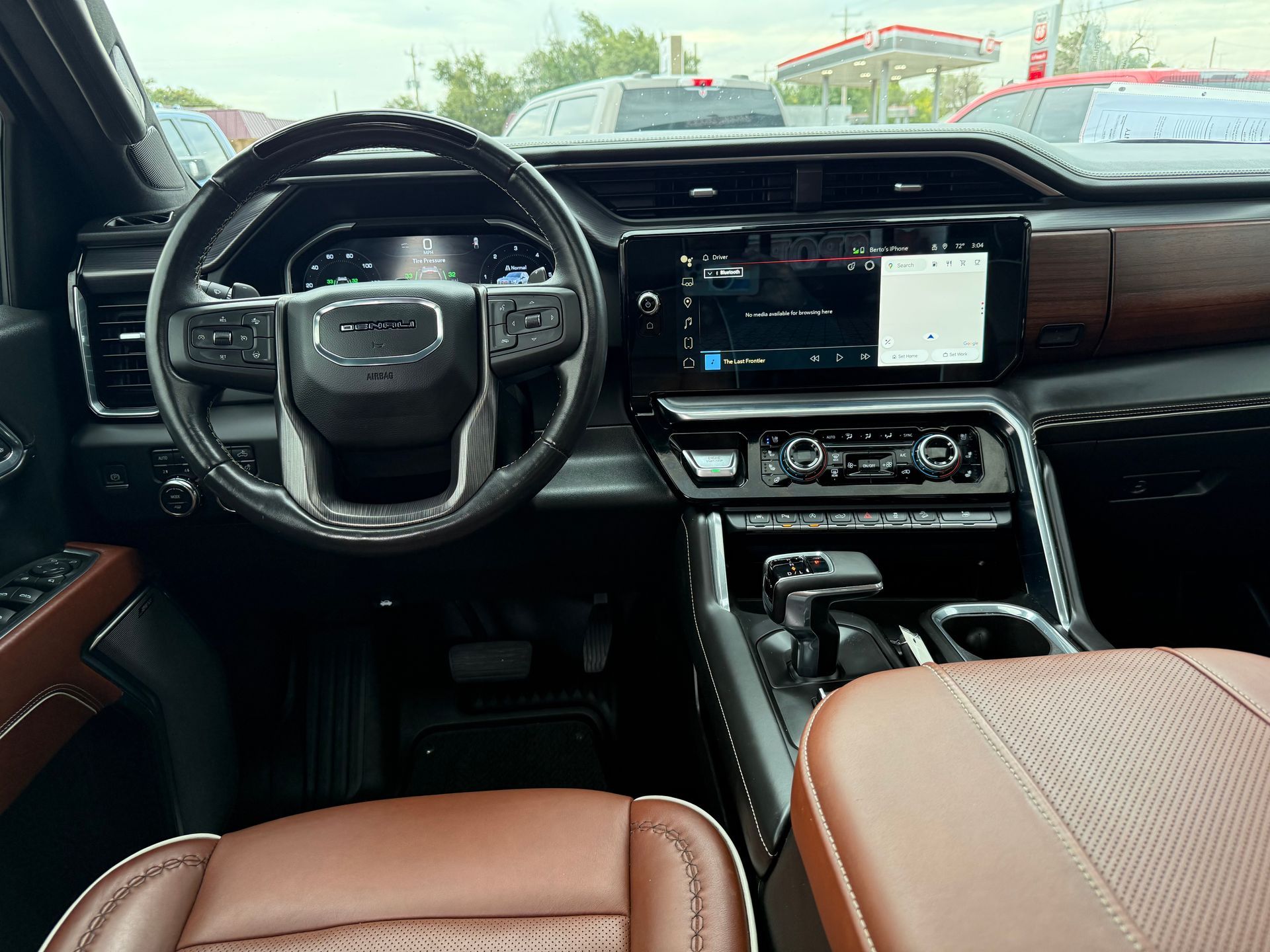 Interior of a GMC truck; brown leather seats, black steering wheel, and large infotainment screen.