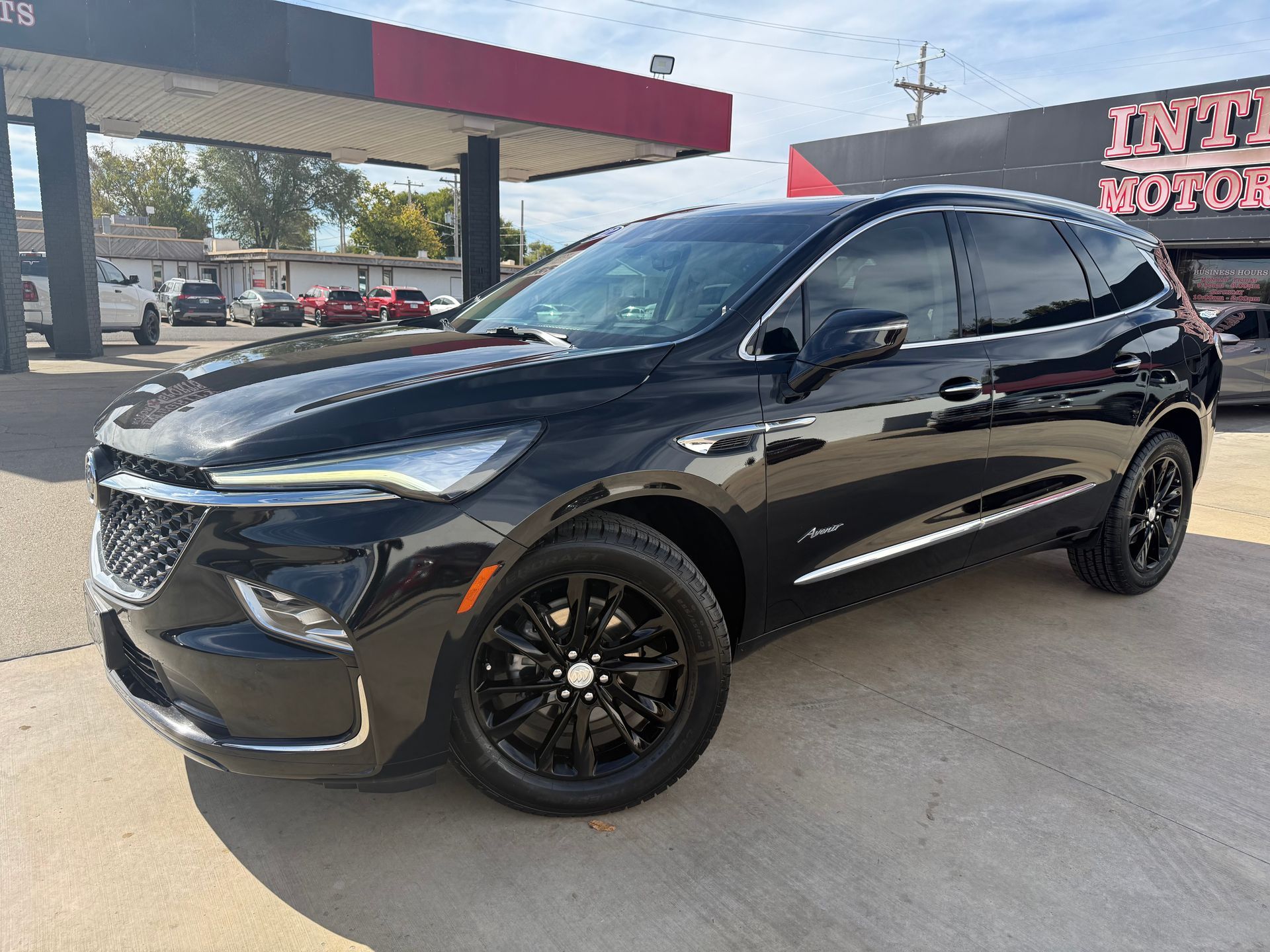 Black Buick Enclave SUV parked on a sunny day in front of an auto shop.