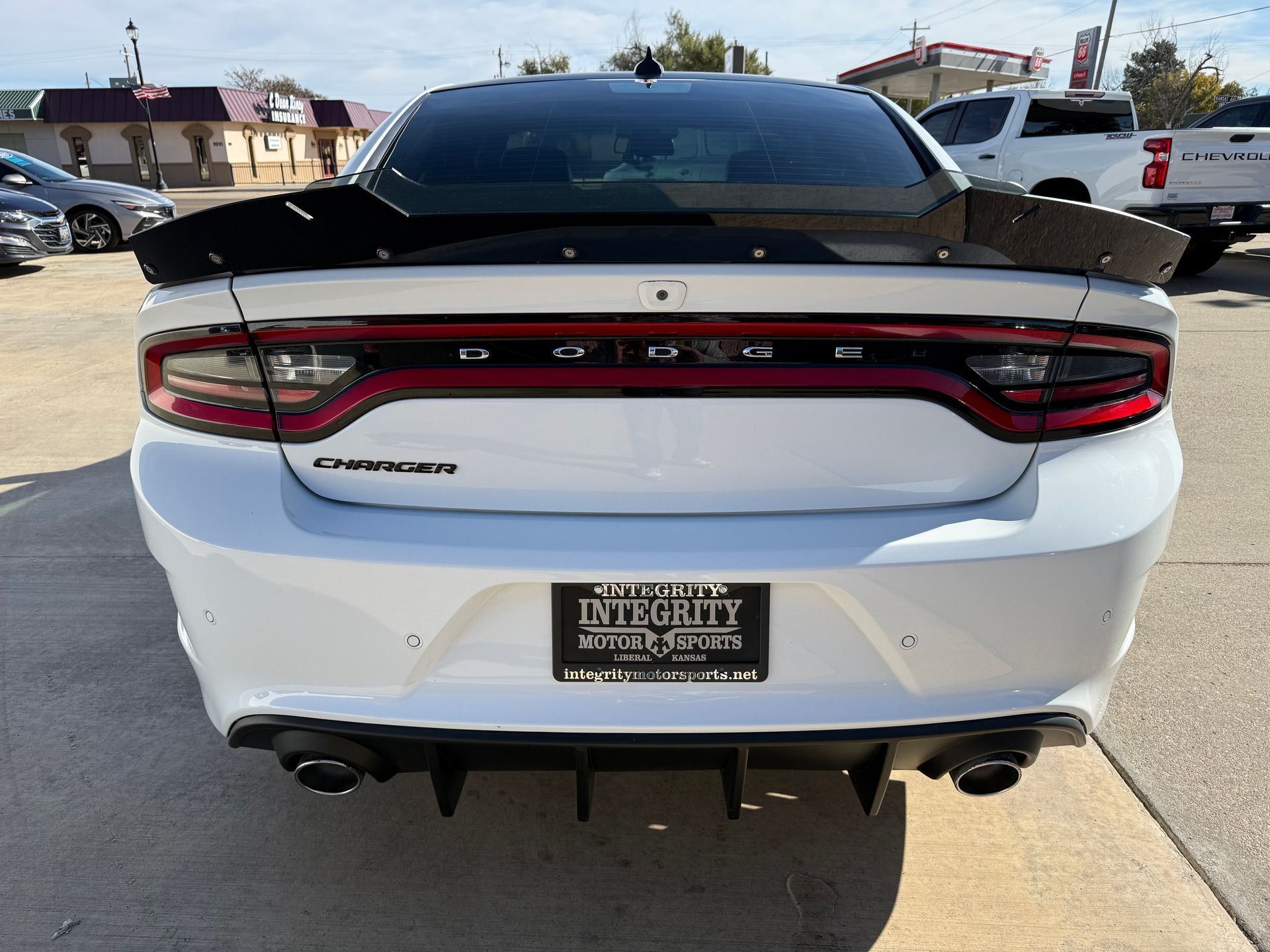 White Dodge Charger with black spoiler and rear diffuser, parked outdoors.