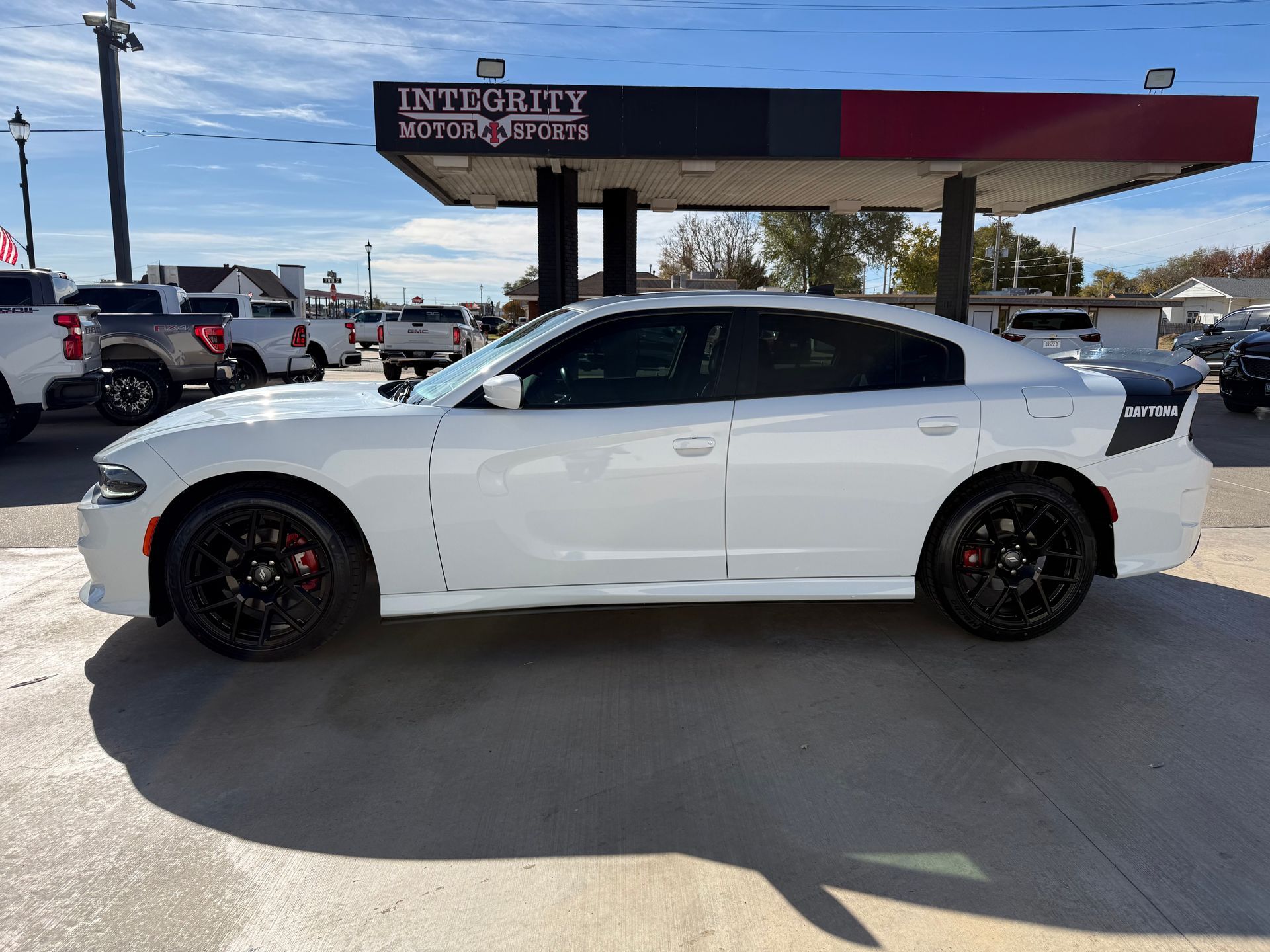 White Dodge Charger at a car dealership. Black rims, red brake calipers.