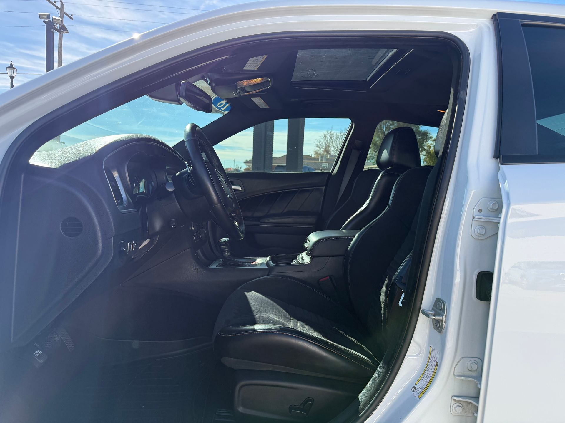 Interior view of a white car with black leather seats, a sunroof, and the driver's side door open.