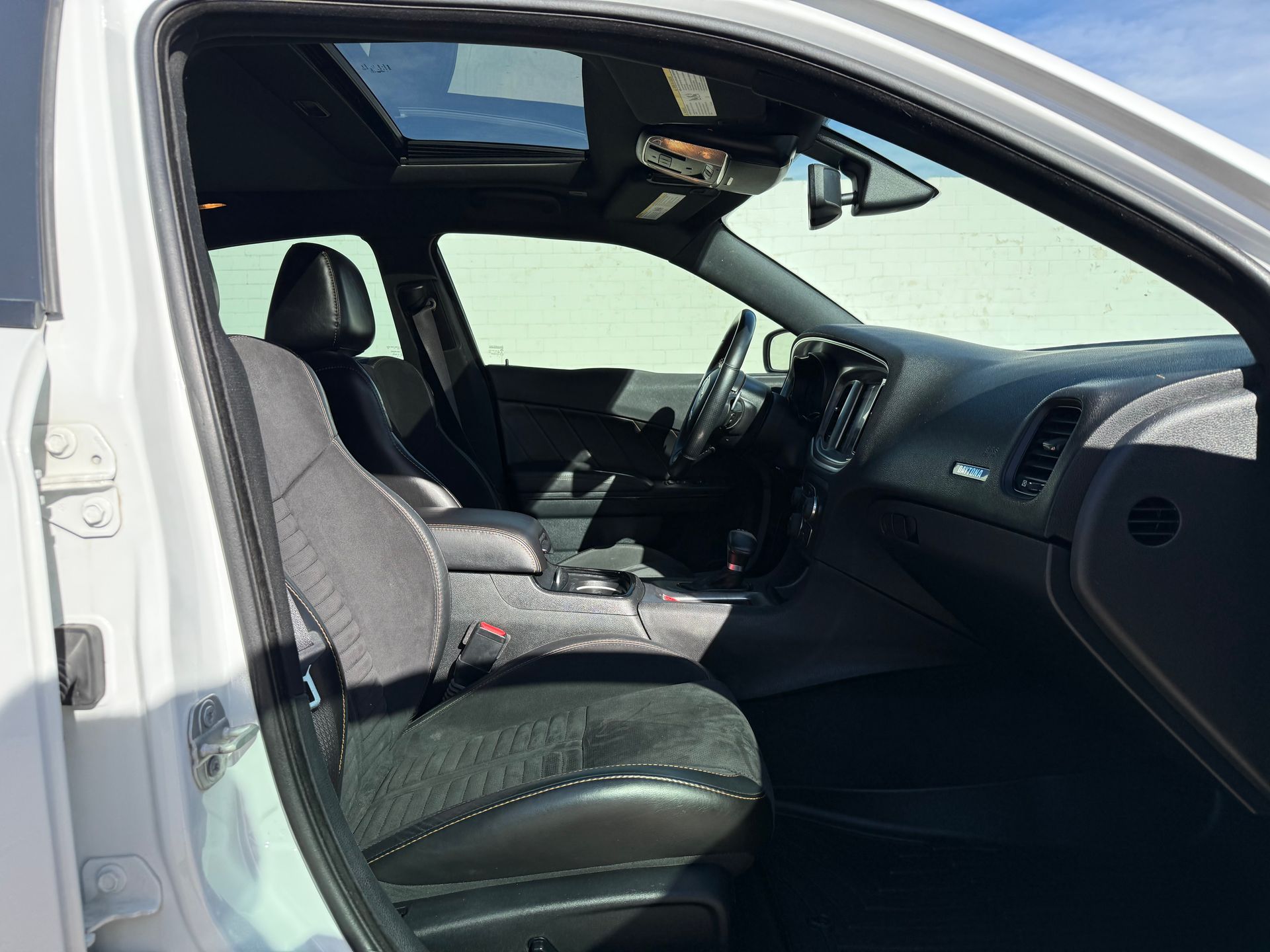 Interior of a white car, front seat visible. Black upholstery, sunroof open, dashboard, and steering wheel in view.