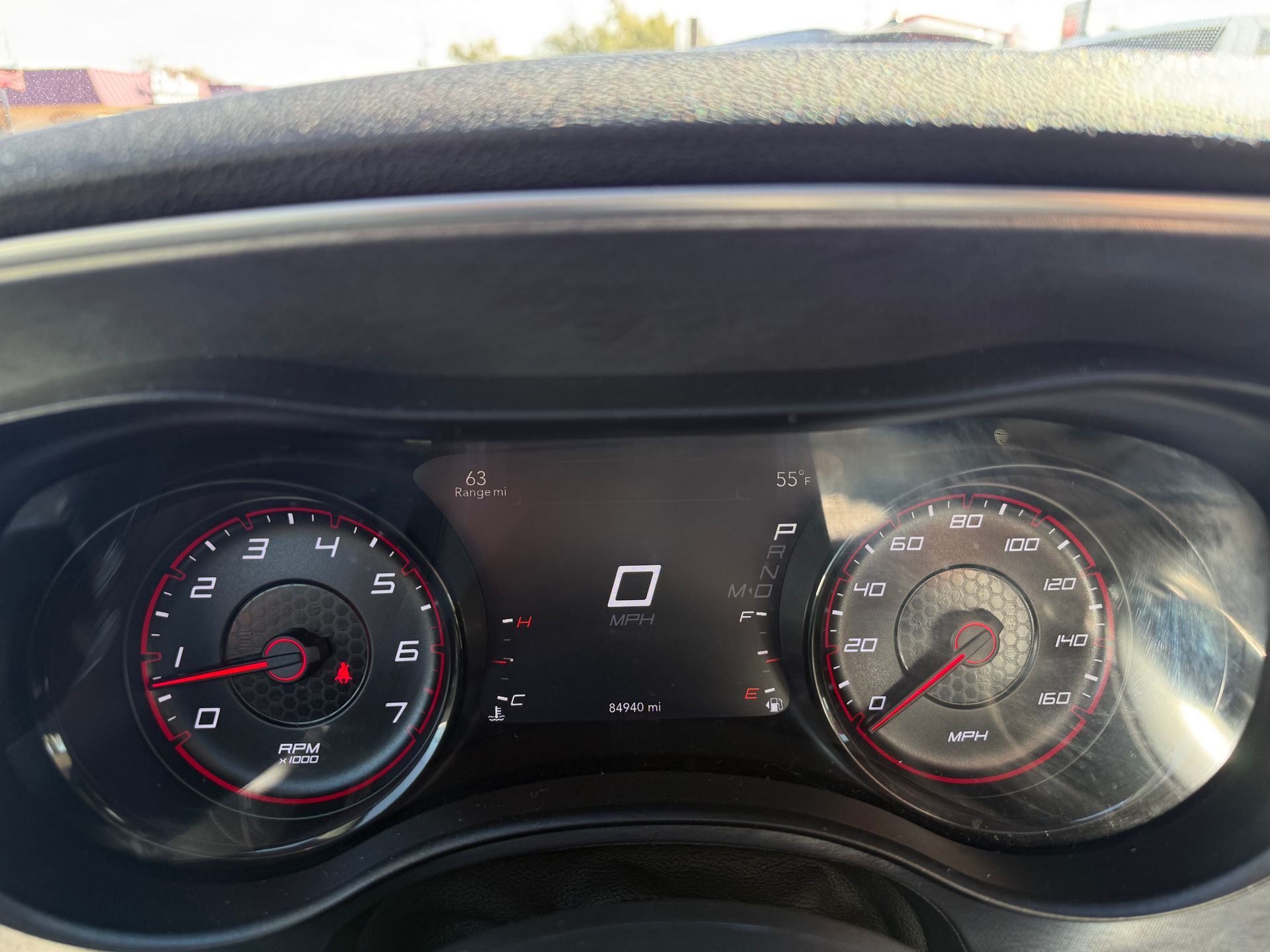 Car dashboard displaying zero speed and other gauges. Red needles and white text on a black background.