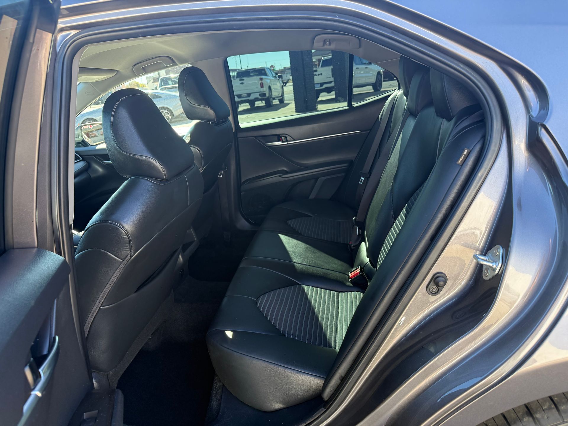 Interior view of a gray car's backseat with black seats. Daylight streams through the windows.