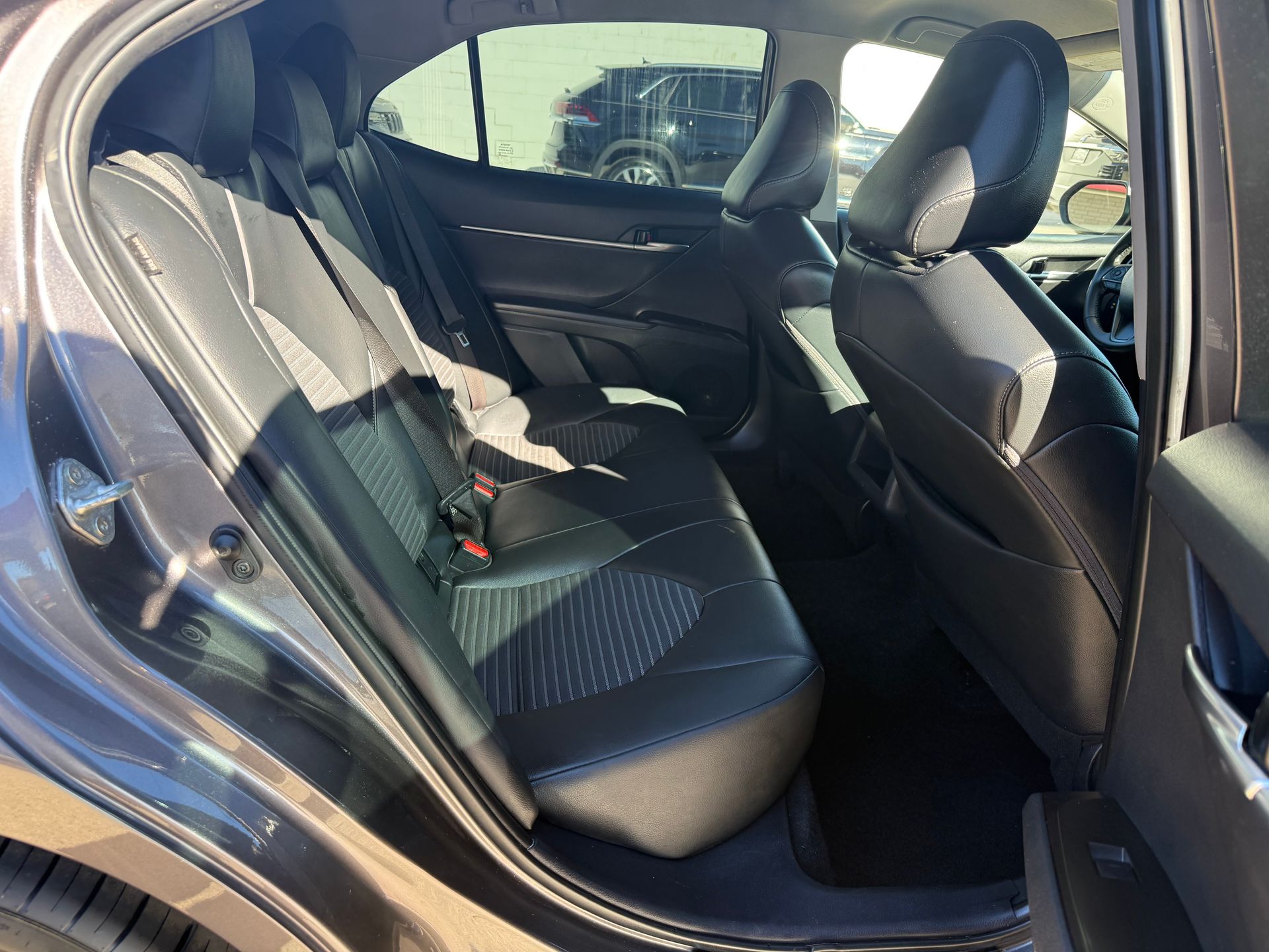 Rear interior of a gray car with black leather seats and white stitching.