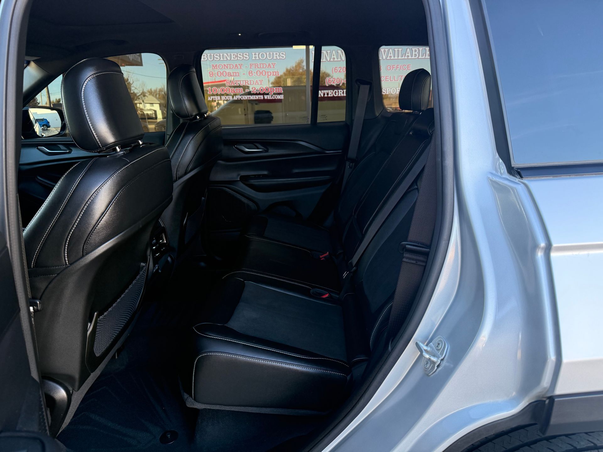 Back interior of a silver SUV, showing black leather seats and open door.