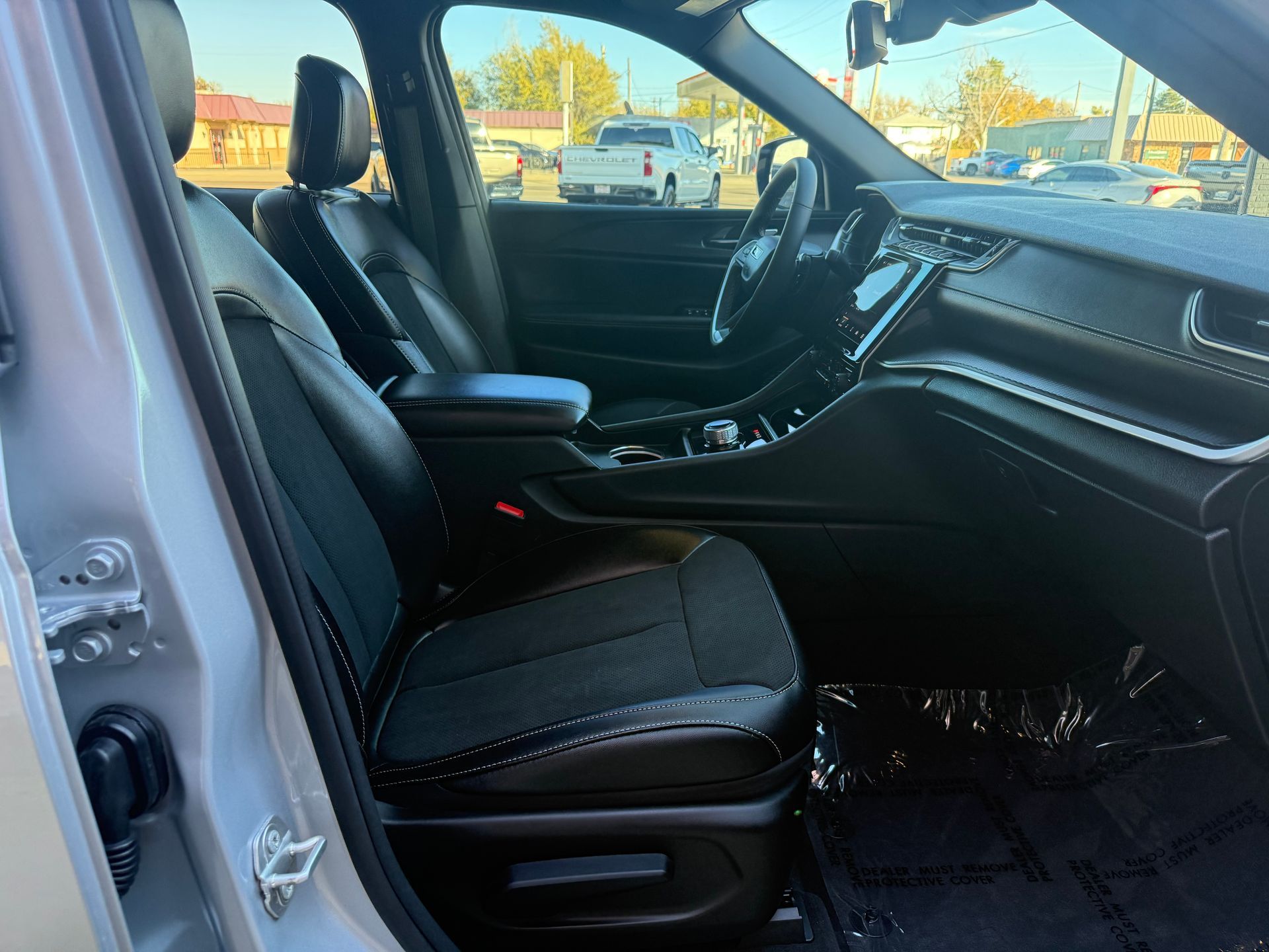 Black leather car interior with black floor mat, steering wheel, and outside view.