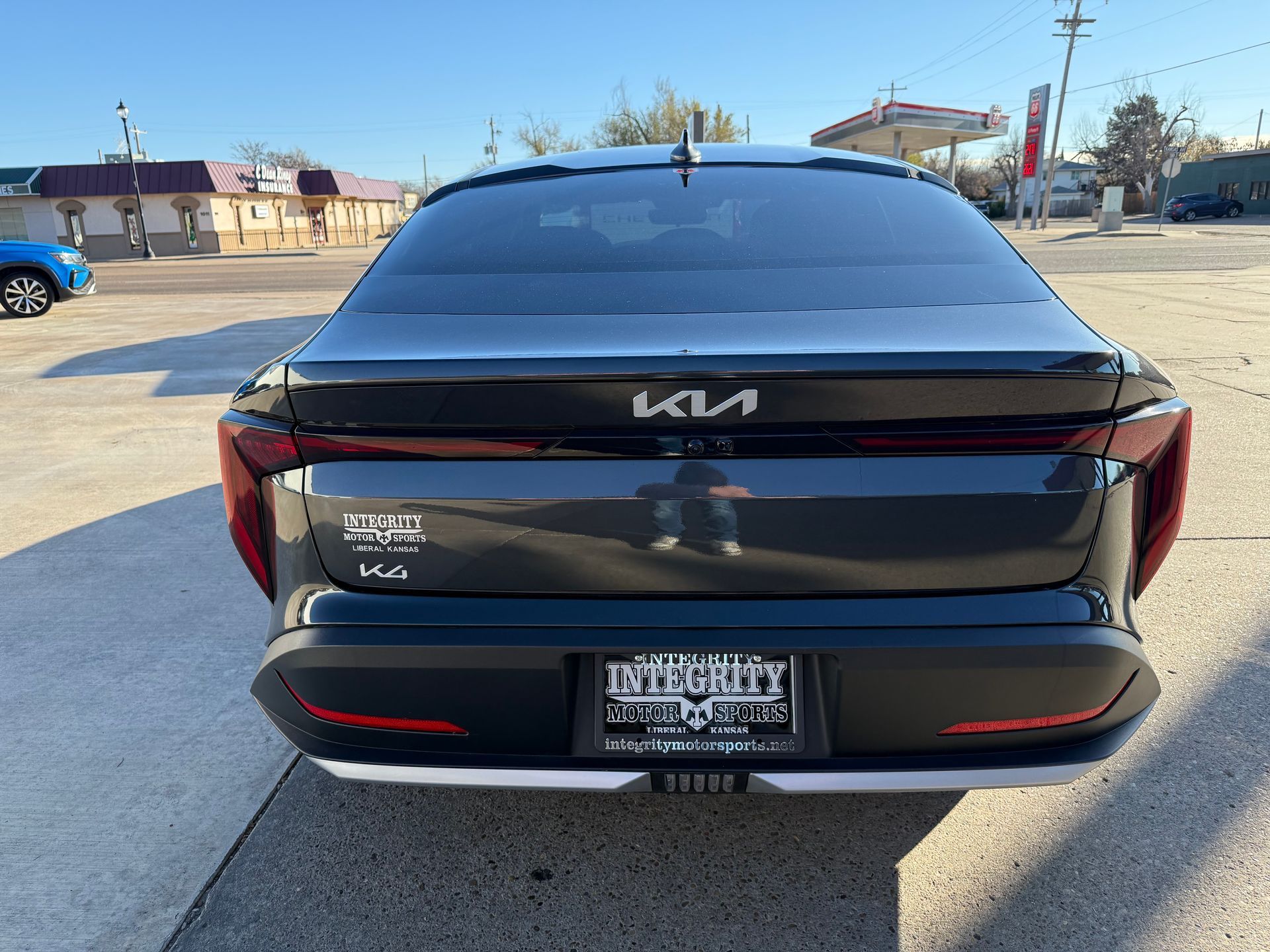 Rear view of a dark gray Kia, parked outdoors, showing the Kia logo and license plate.