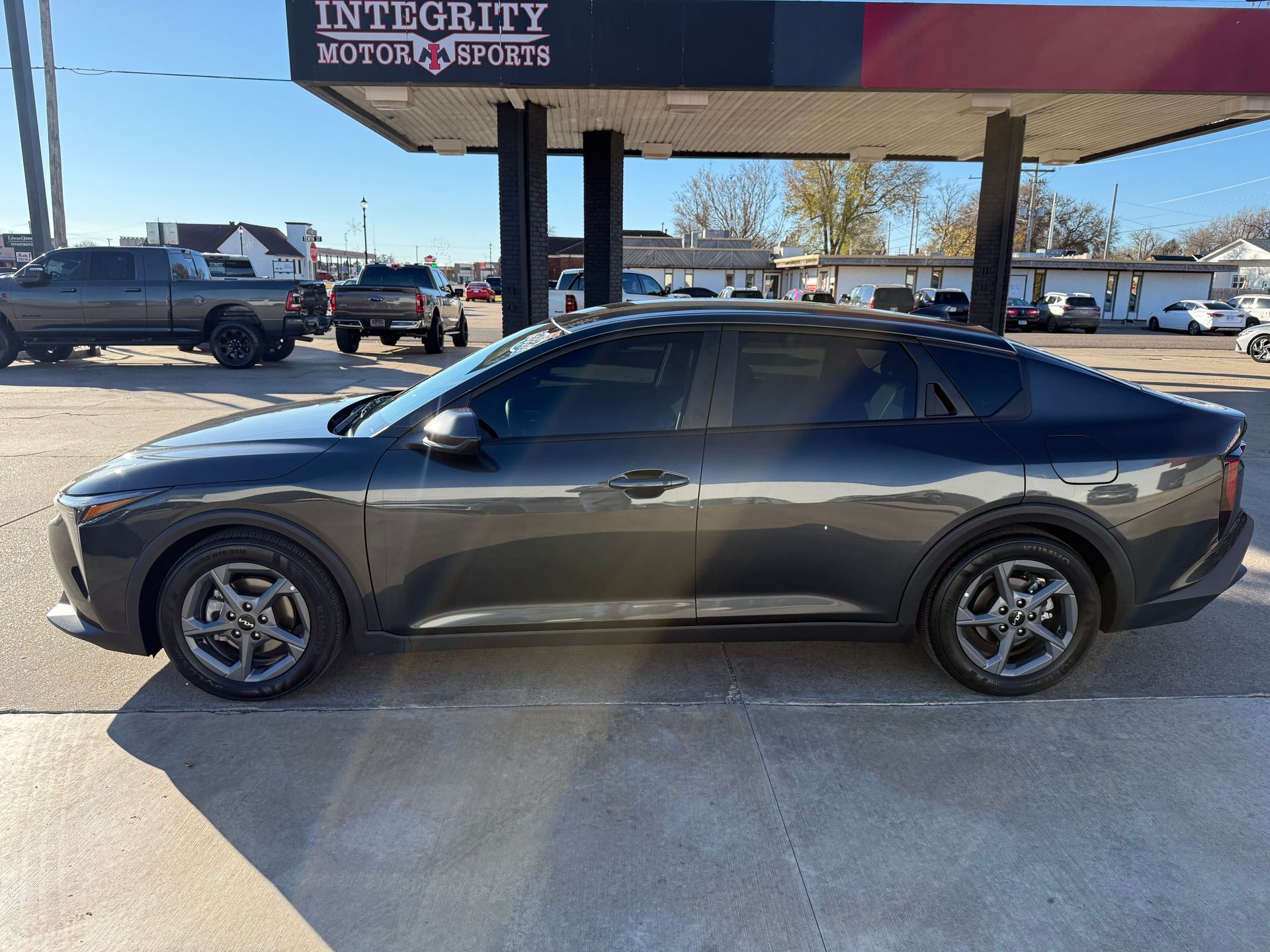 Dark gray Kia K5 sedan parked at a car dealership on a sunny day.