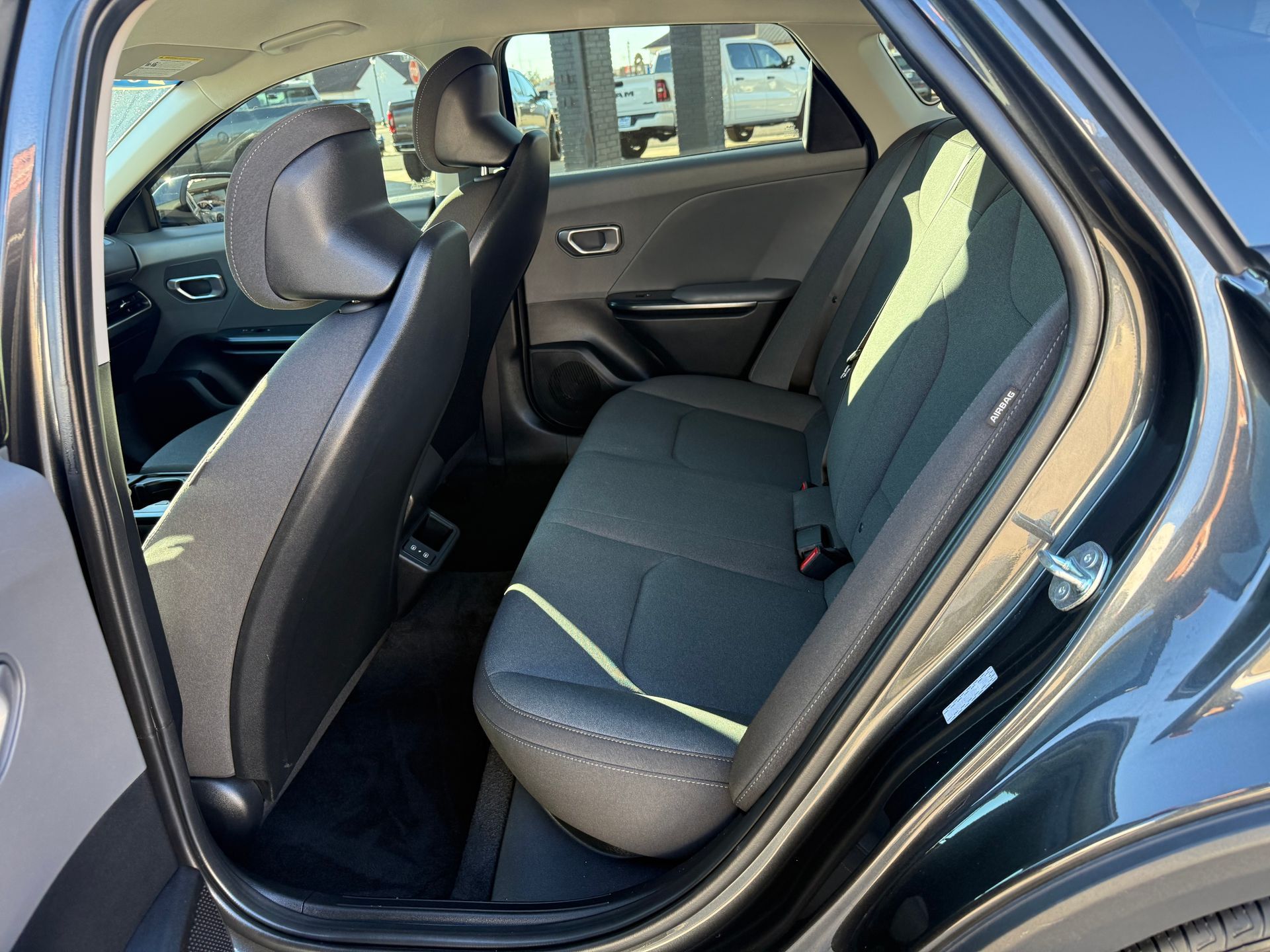 Interior view of a dark-colored car's rear seats. The seats are gray with black headrests, and the door is open.