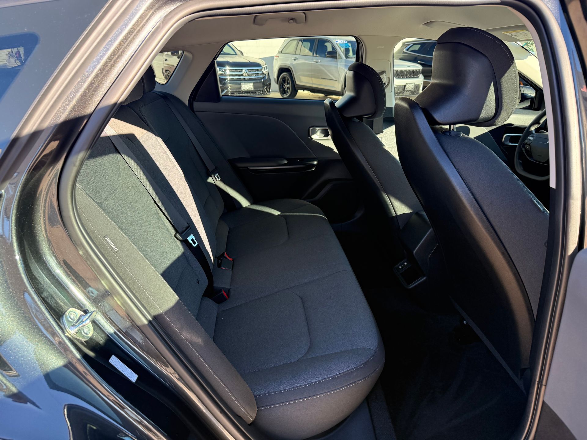 Interior view of a car's back seat, featuring gray fabric seats and headrests, showing a dark floor.