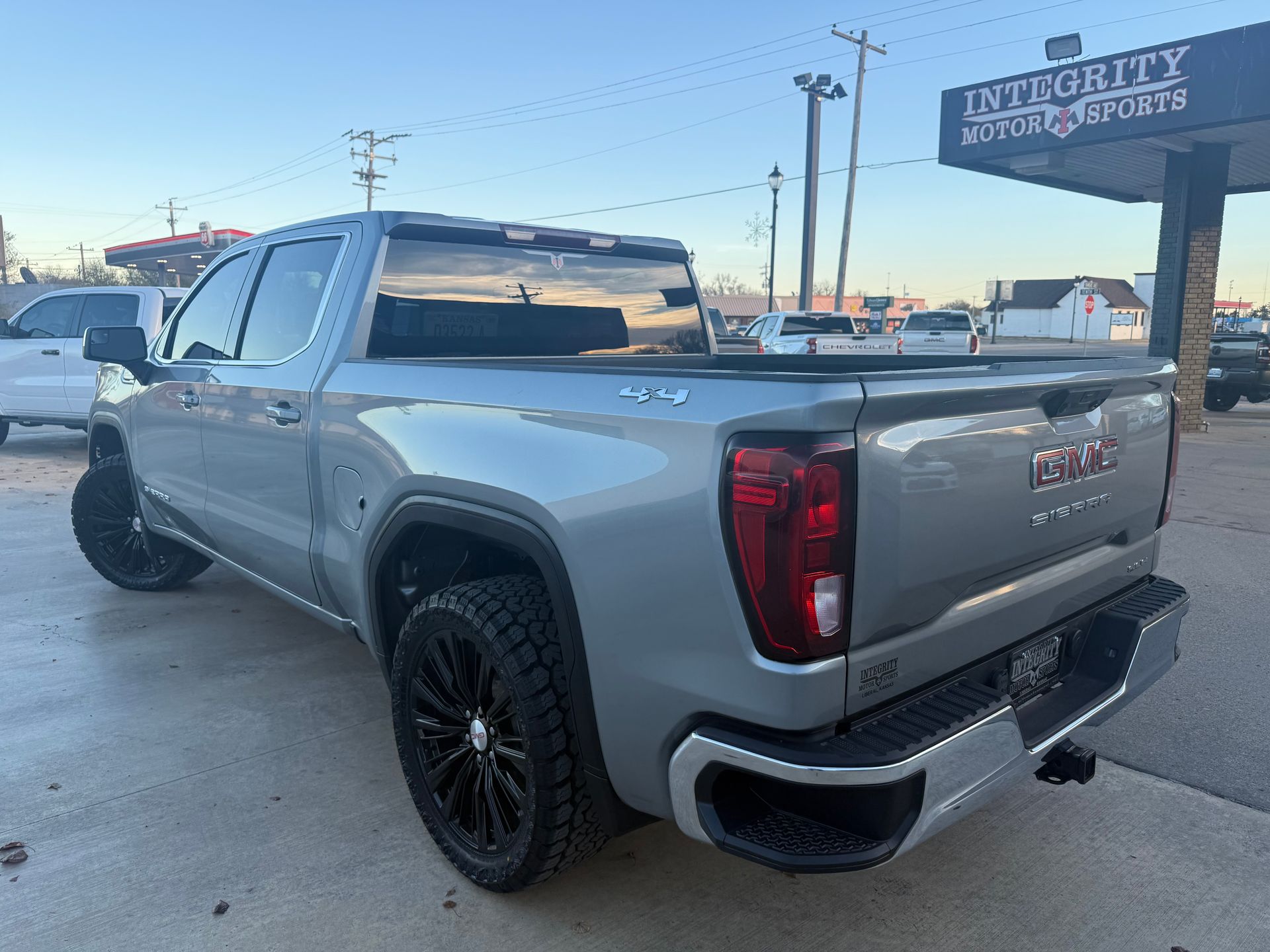Gray GMC Sierra truck with black wheels parked outside a dealership.