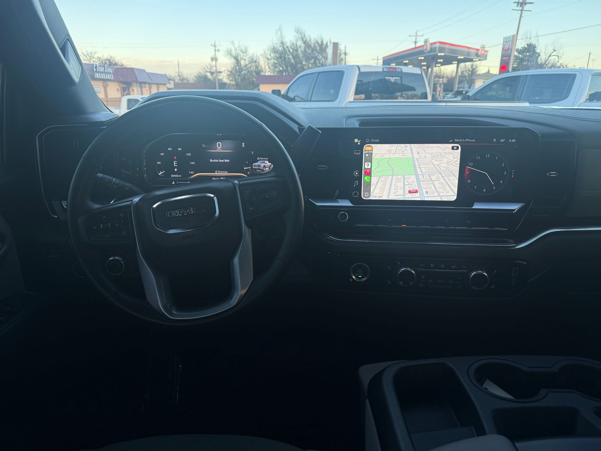 Interior view of a GMC truck dashboard with the steering wheel, navigation screen, and cup holders.