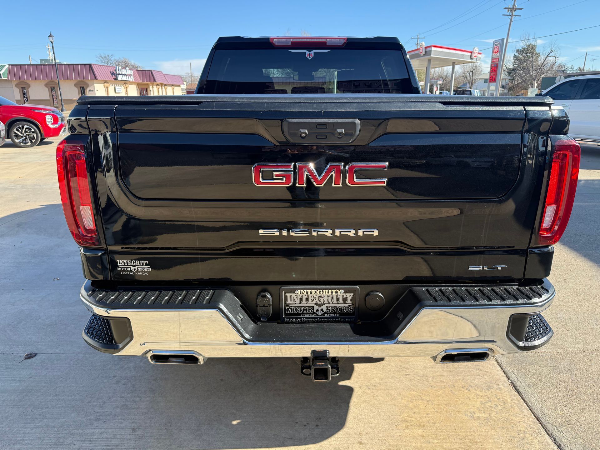 Black GMC Sierra pickup truck's rear view. Features GMC emblem, chrome bumper, and trailer hitch, parked outside.