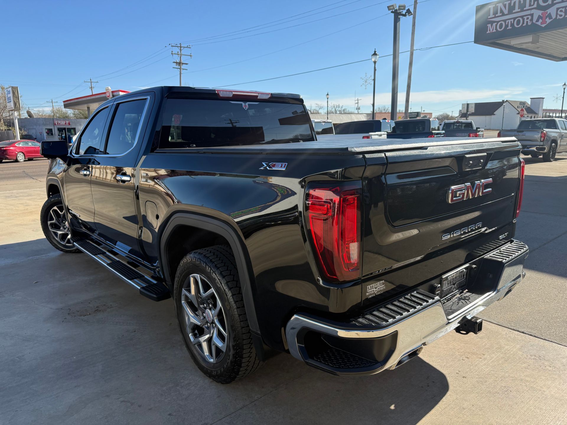 Black GMC Sierra truck with a tonneau cover parked outside a car dealership.