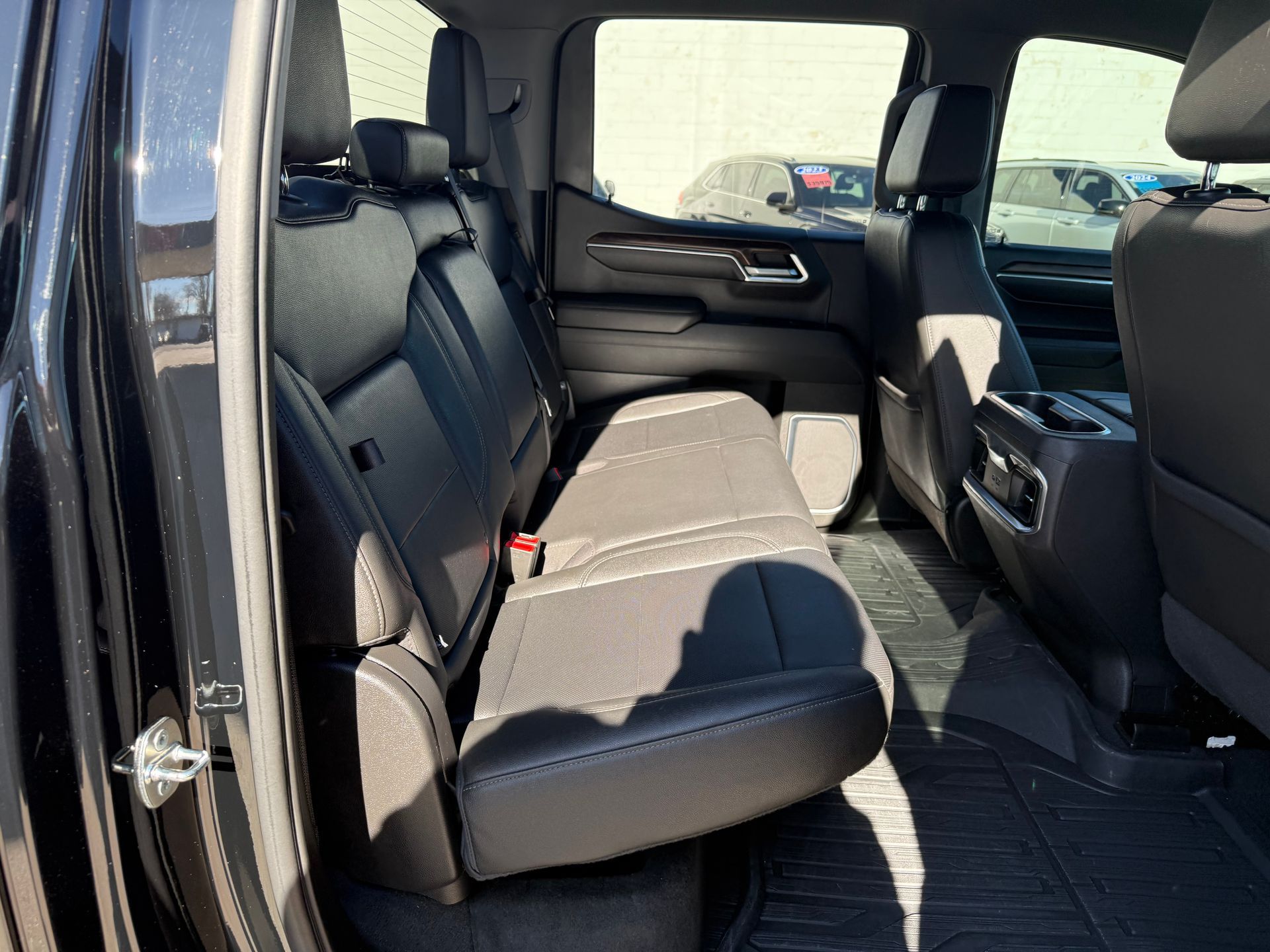 Inside of a black truck's back seat, featuring black seats, floor mats, and windows looking out.