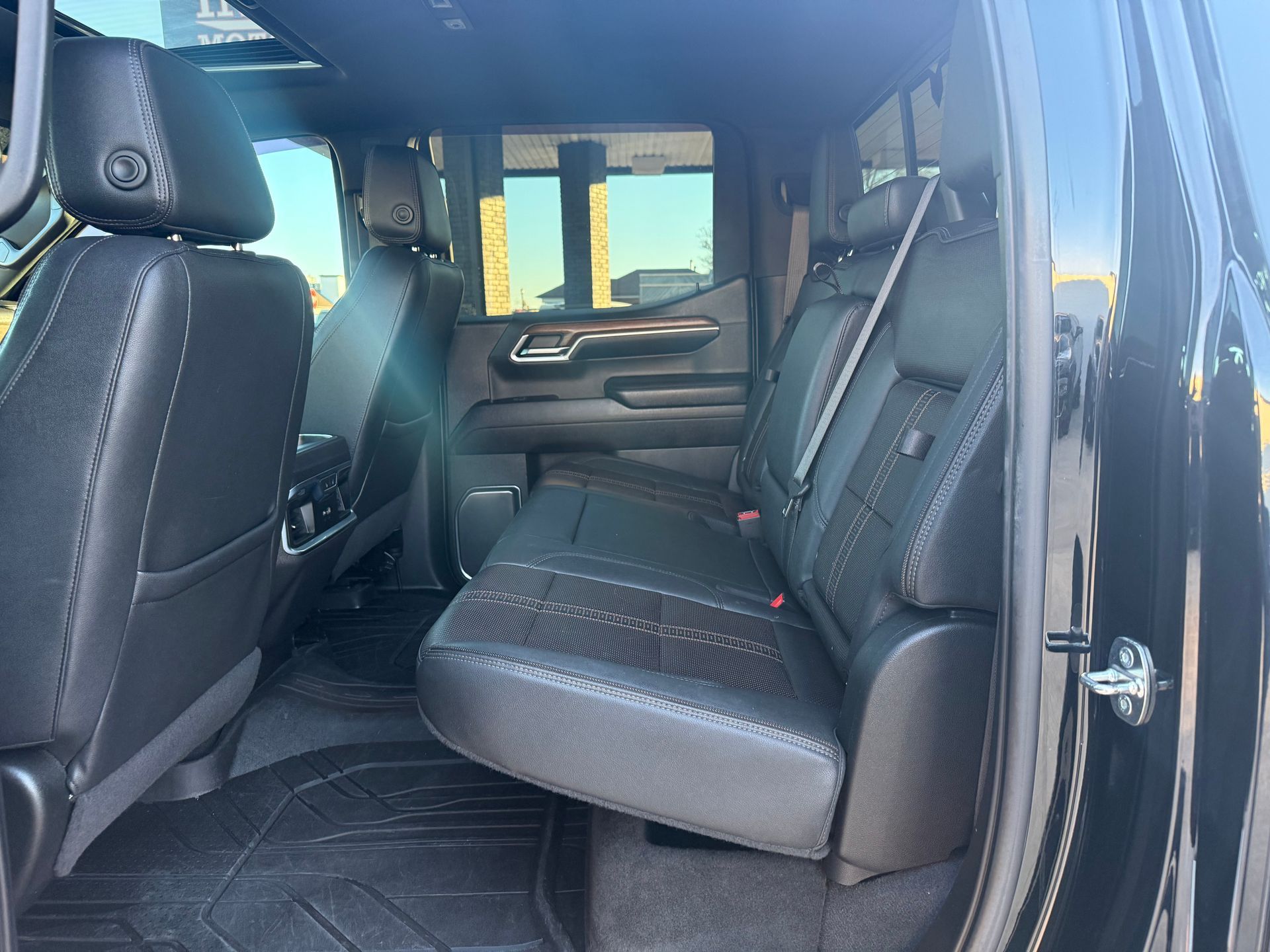 Interior of a black pickup truck's back seat, showing black leather seats, a window, and dark flooring.
