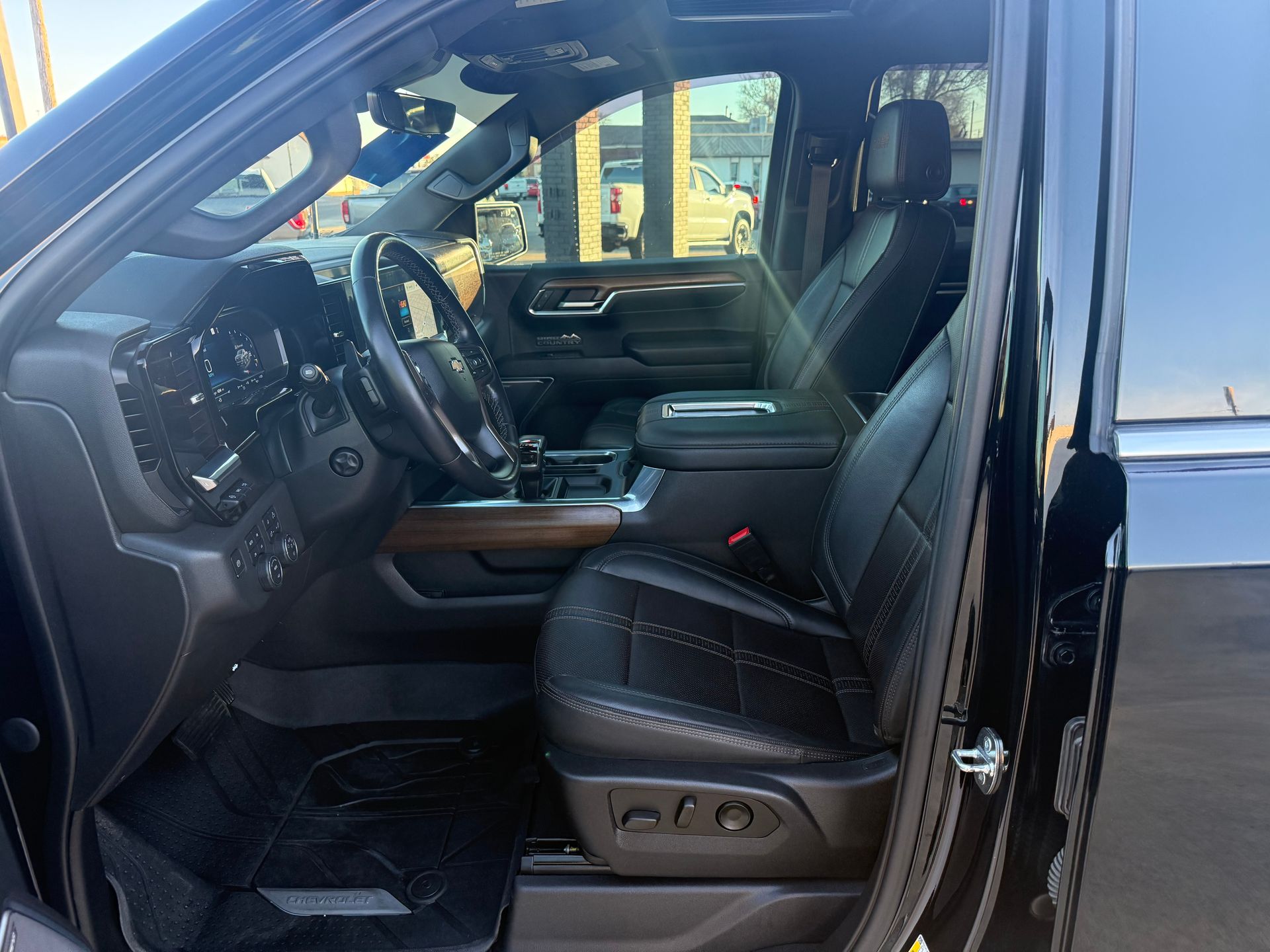 Black truck interior, driver's seat visible. Black leather seats, dashboard, steering wheel. Sunlight.