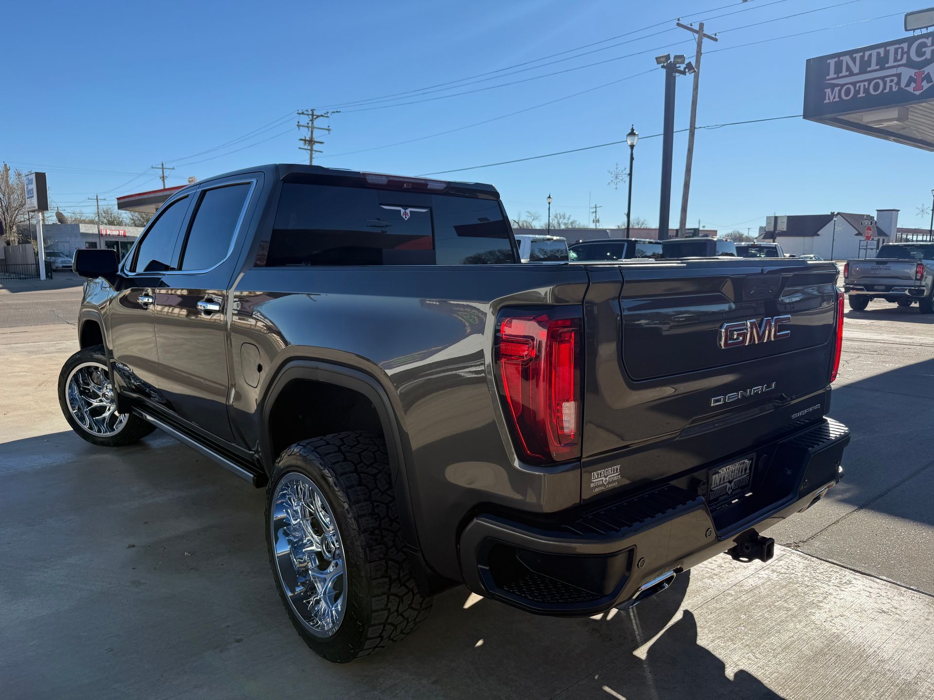 Dark gray GMC truck with chrome wheels parked outside a dealership on a sunny day.