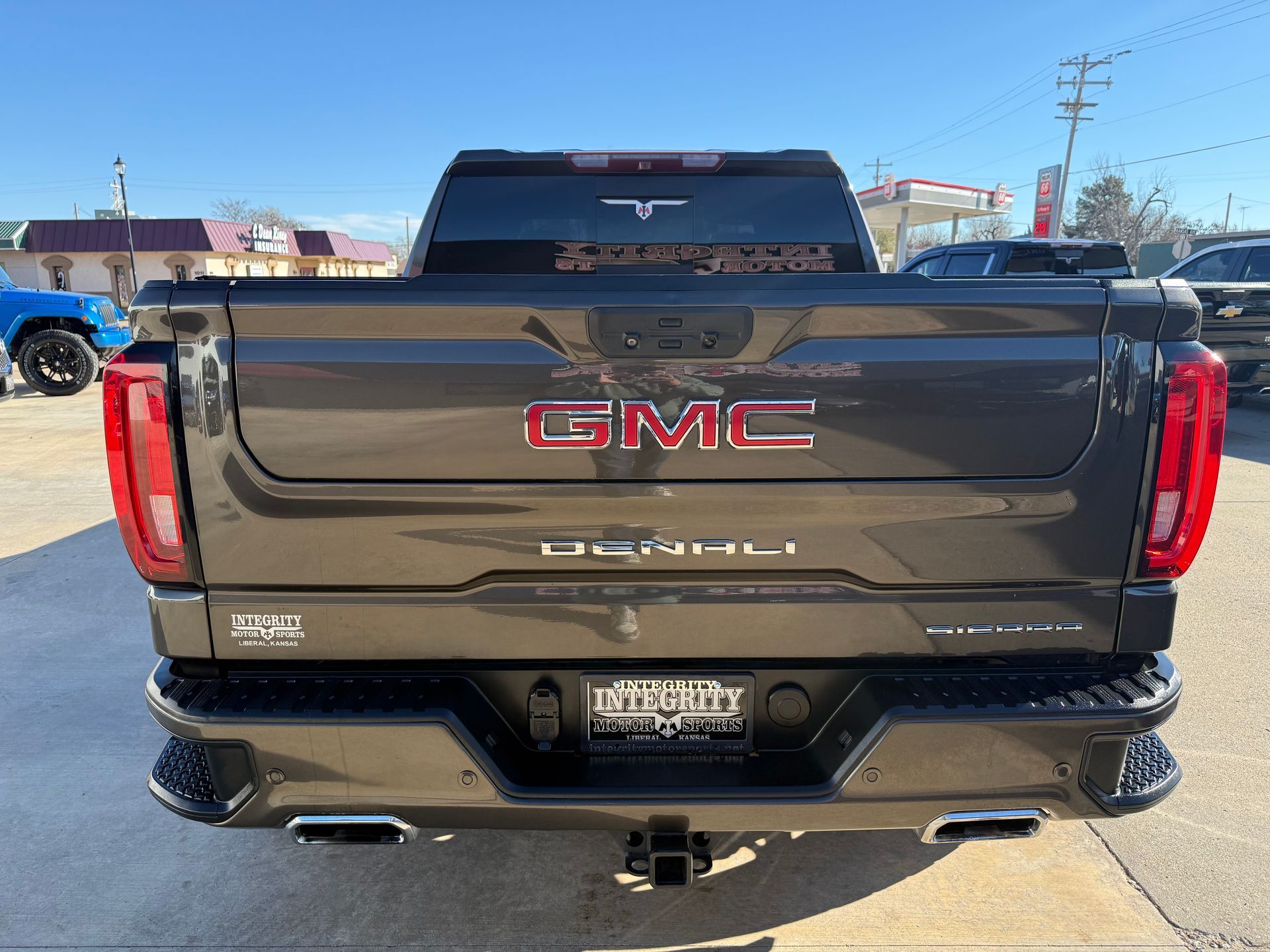 Rear view of a dark gray GMC Denali truck with red GMC logo and black bumper, parked on a sunny day.