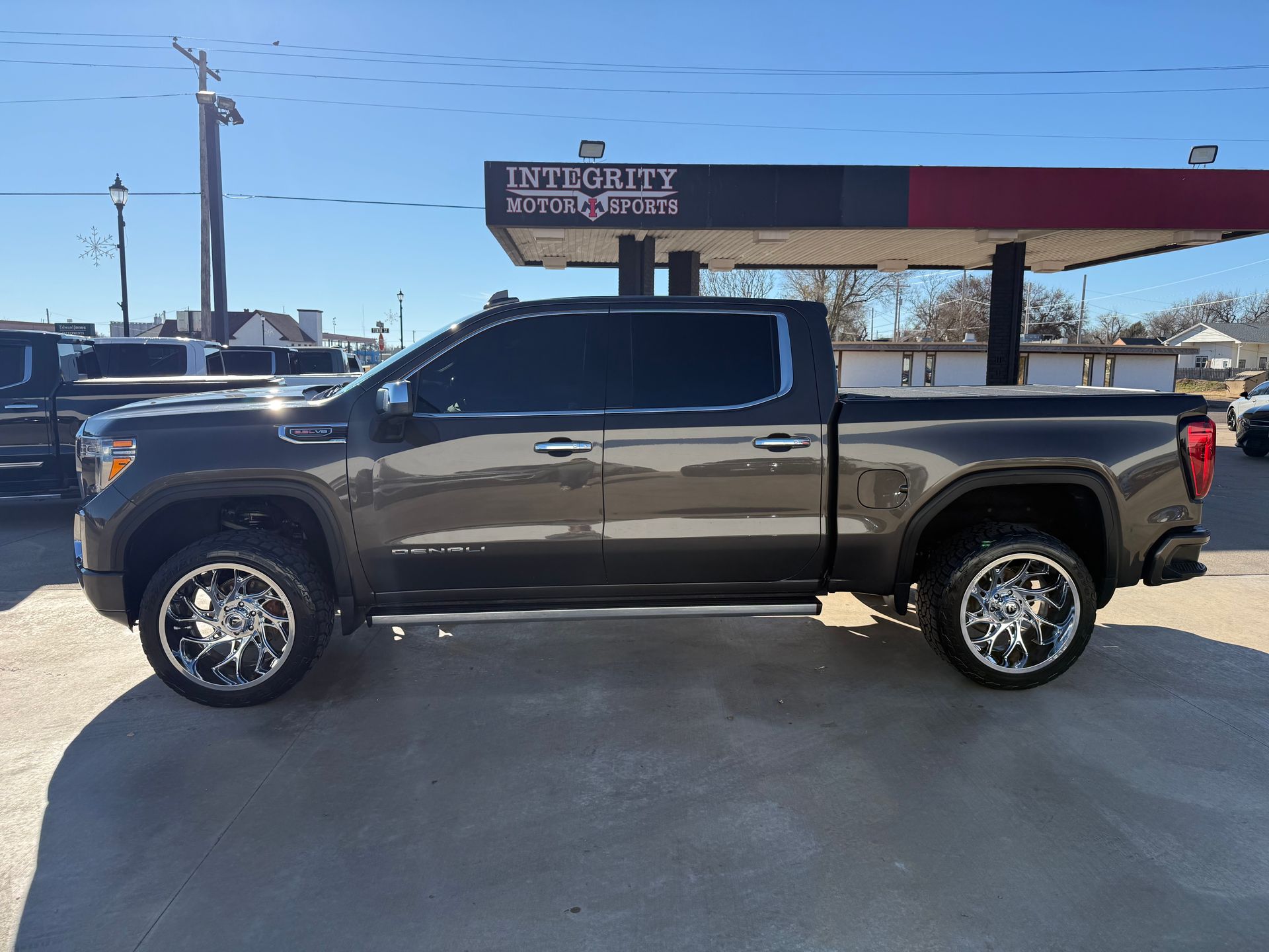 Dark gray pickup truck with chrome rims parked outside a business with a gas pump canopy.