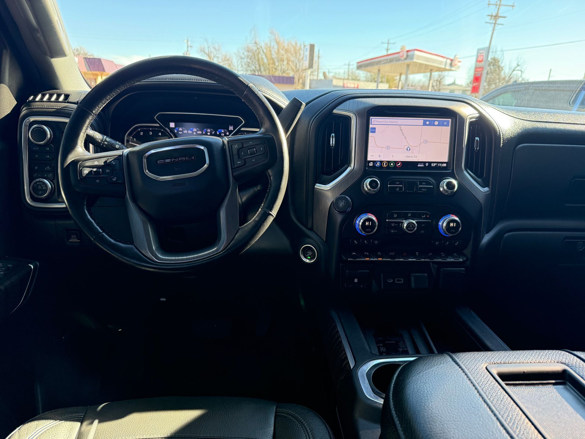 Interior of a GMC truck, showing steering wheel, dashboard with screen displaying navigation, and center console.