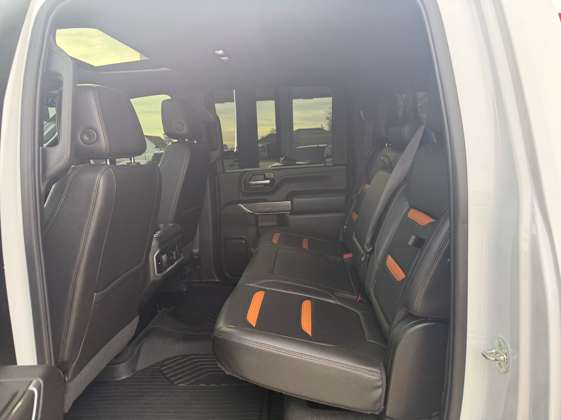 Interior of a gray truck showing black leather seats with orange accents; sunlight streams in.