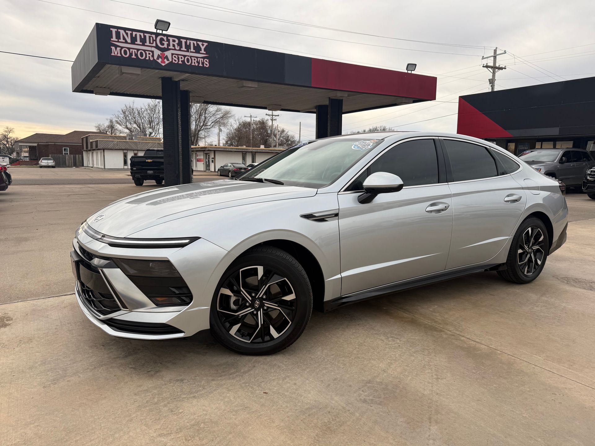 Red Nissan Altima sedan parked at a car dealership on a sunny day.