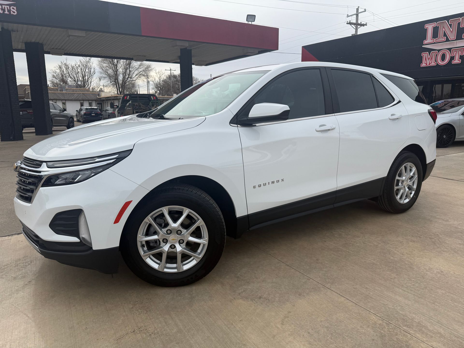 Tan GMC Terrain SUV with black wheels parked outside a car dealership on a sunny day.