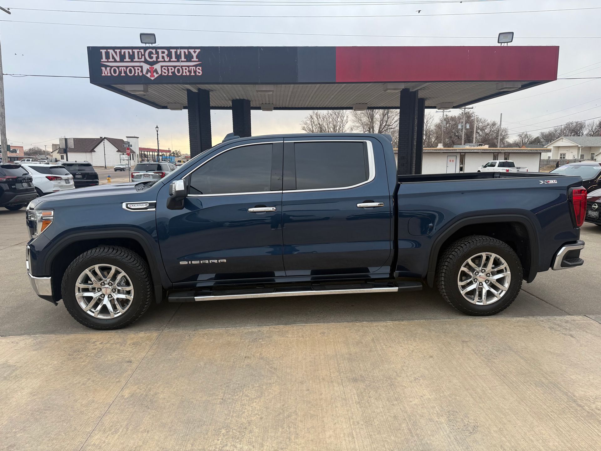 Blue GMC Sierra truck parked at a car dealership under a canopy.