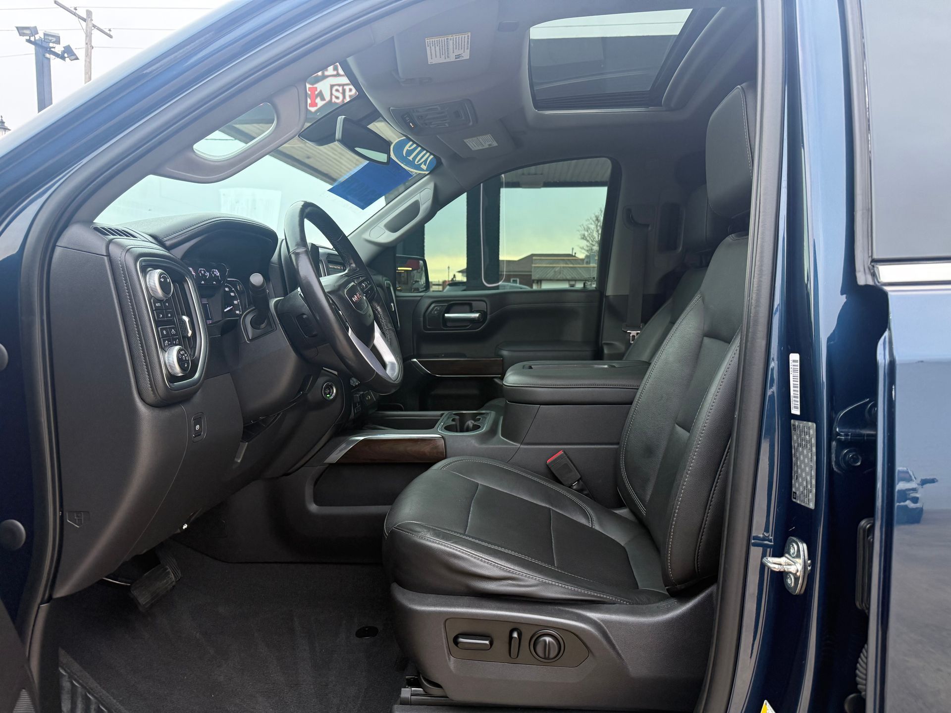 Interior view of a blue truck with black leather seats, sunroof, and steering wheel; door open.