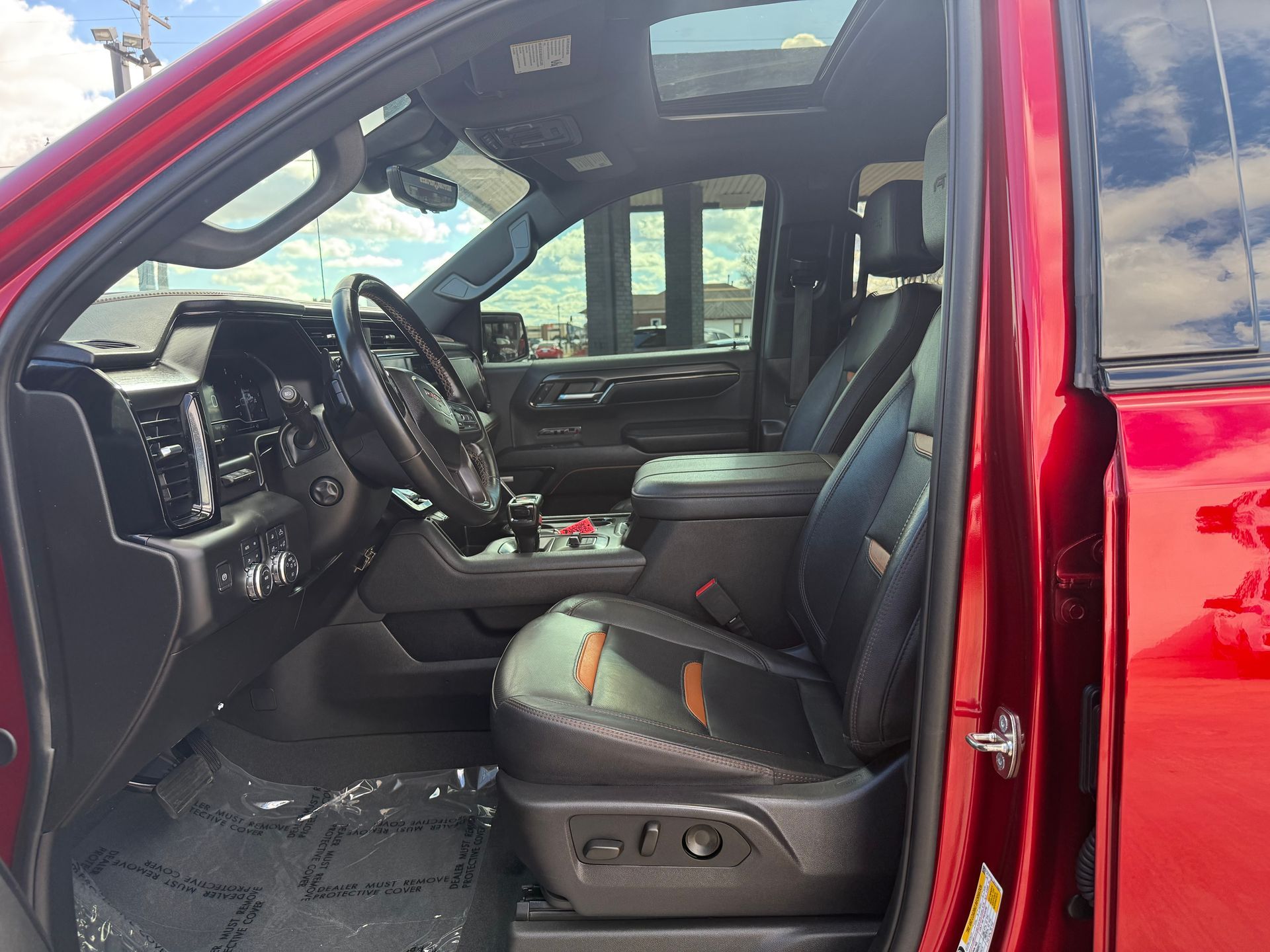 Red truck interior with black leather seats, steering wheel, and console. Open door.