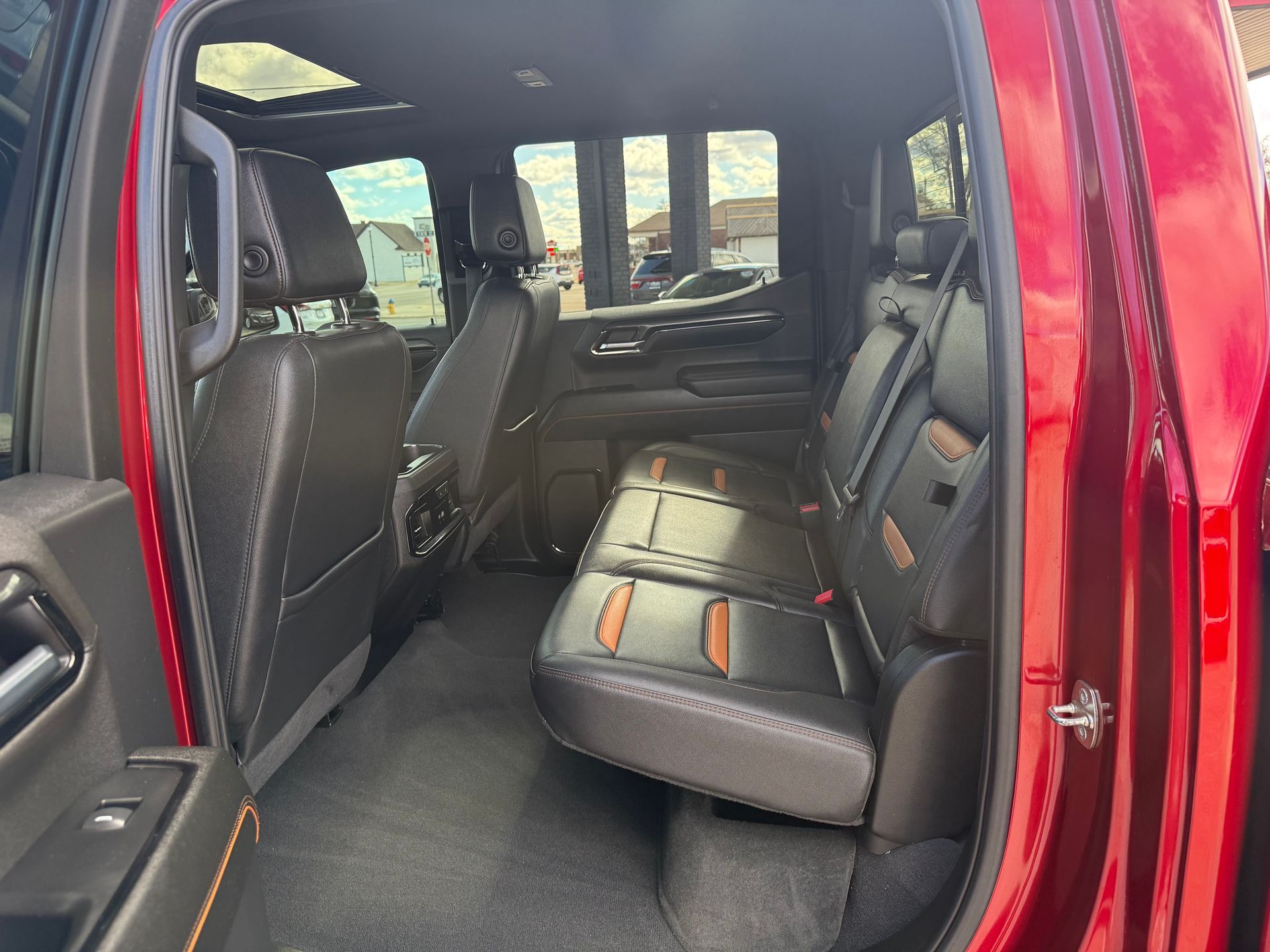 Interior view of a red truck's back seat with black leather seats and a sunroof.