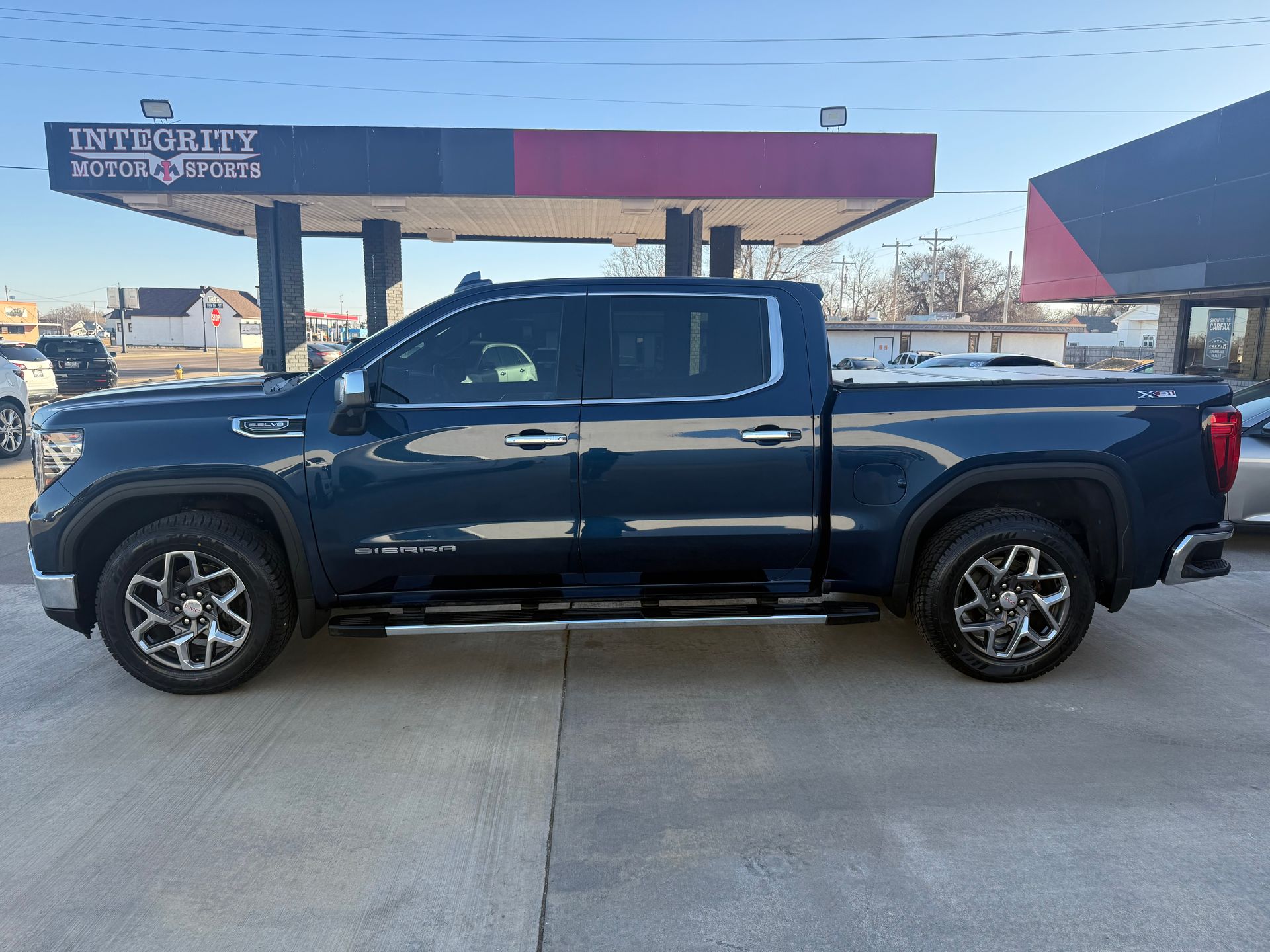 Blue GMC Sierra truck parked in front of a building with a red and blue canopy.