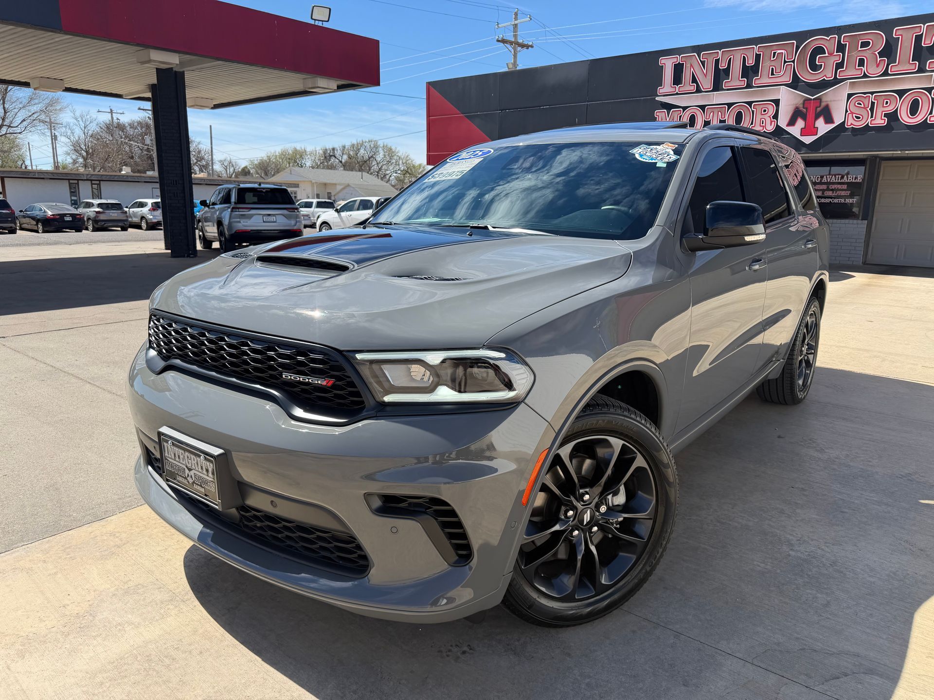 Gray Dodge Durango SUV parked outside a dealership with a red and white sign.