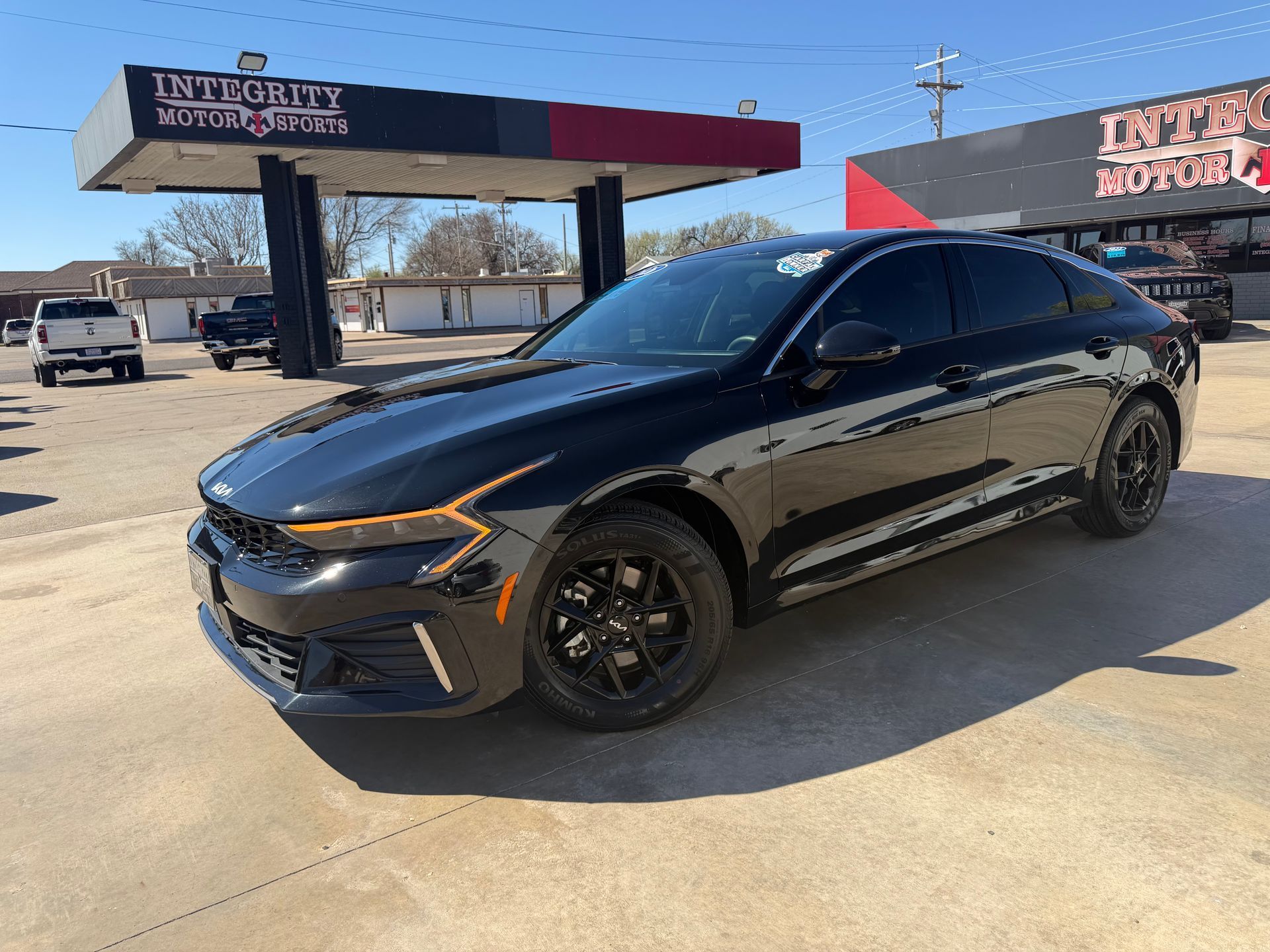Red Nissan Altima sedan parked at a car dealership on a sunny day.