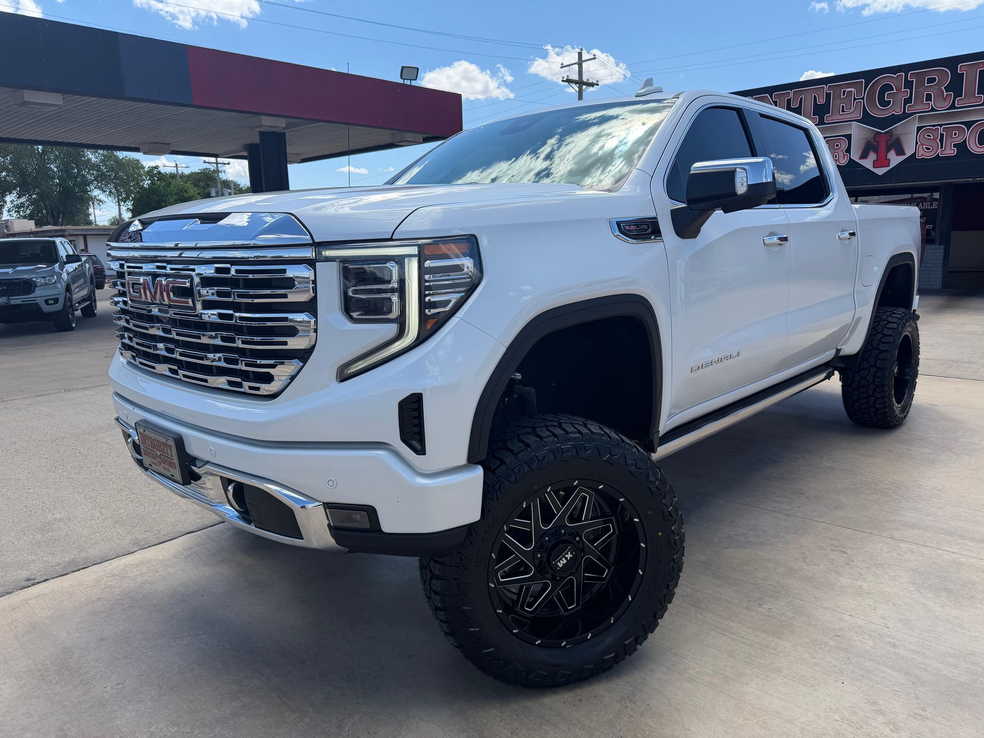 Black Chevrolet Silverado truck in front of a dealership with chrome accents and bright headlights.