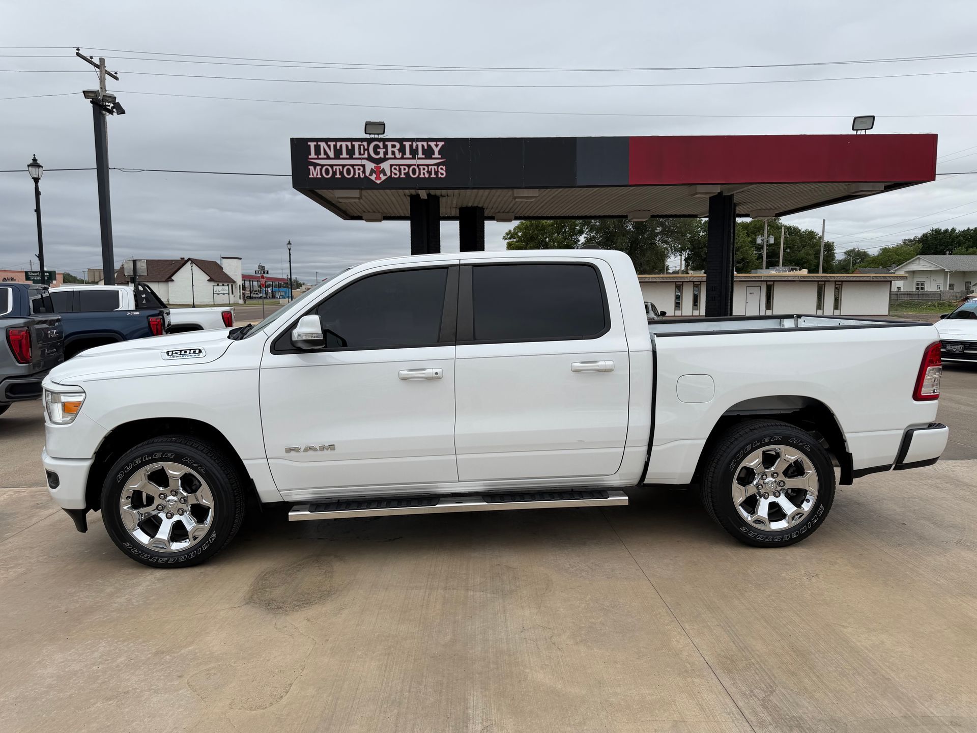 White pickup truck parked on wet pavement in front of a gas station canopy under gray skies