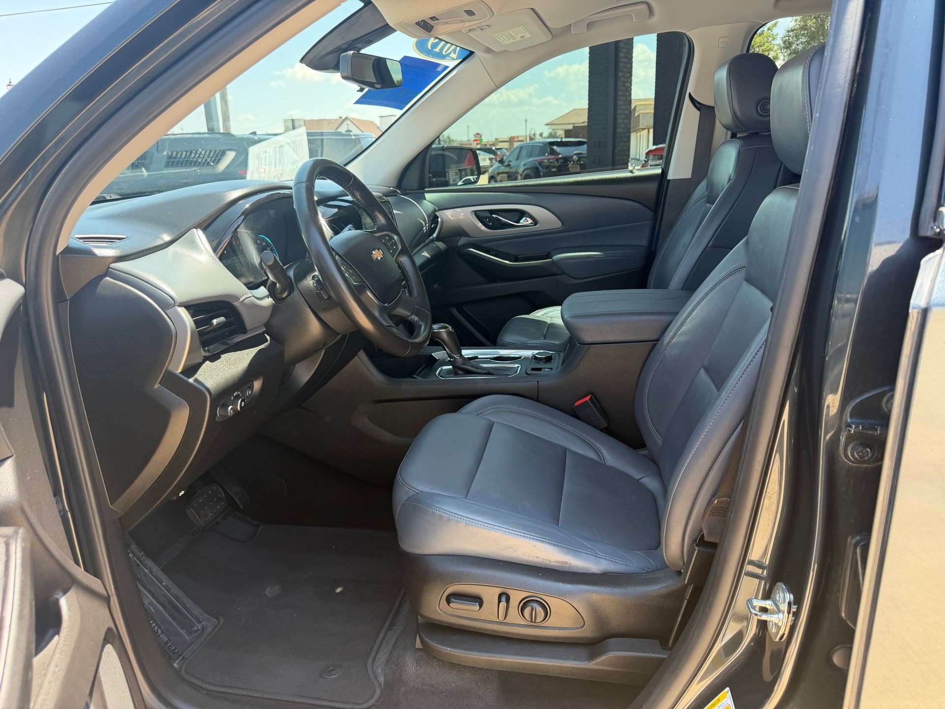 Open driver’s door showing a black leather car interior with steering wheel and front seat.