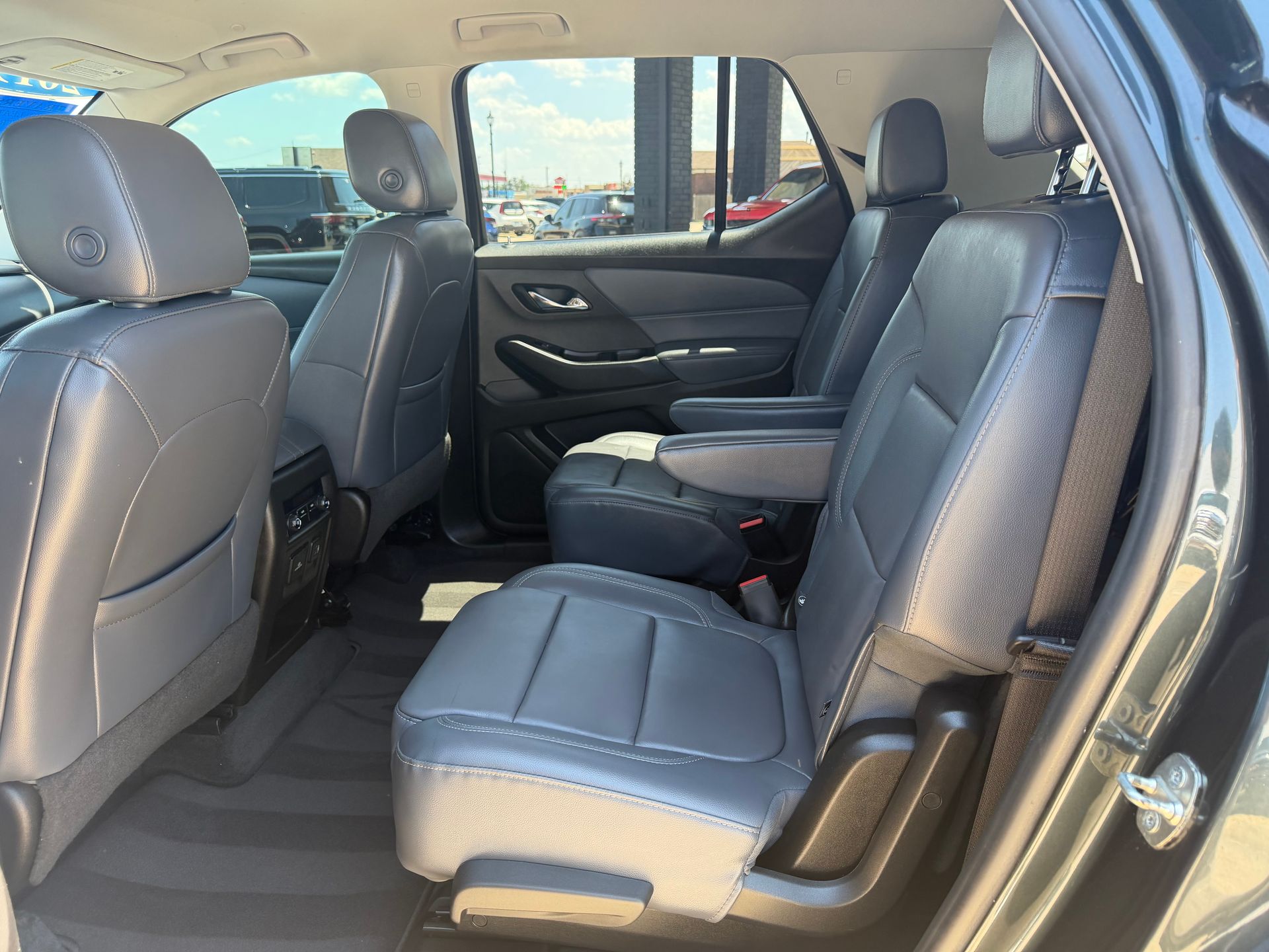Car interior with rear seats folded down, showing black leather upholstery and open door.