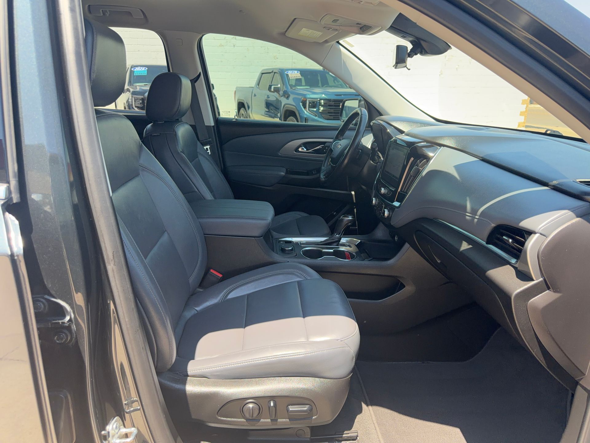 Front passenger view of a car interior with gray leather seats and black dashboard, sunlight streaming in.