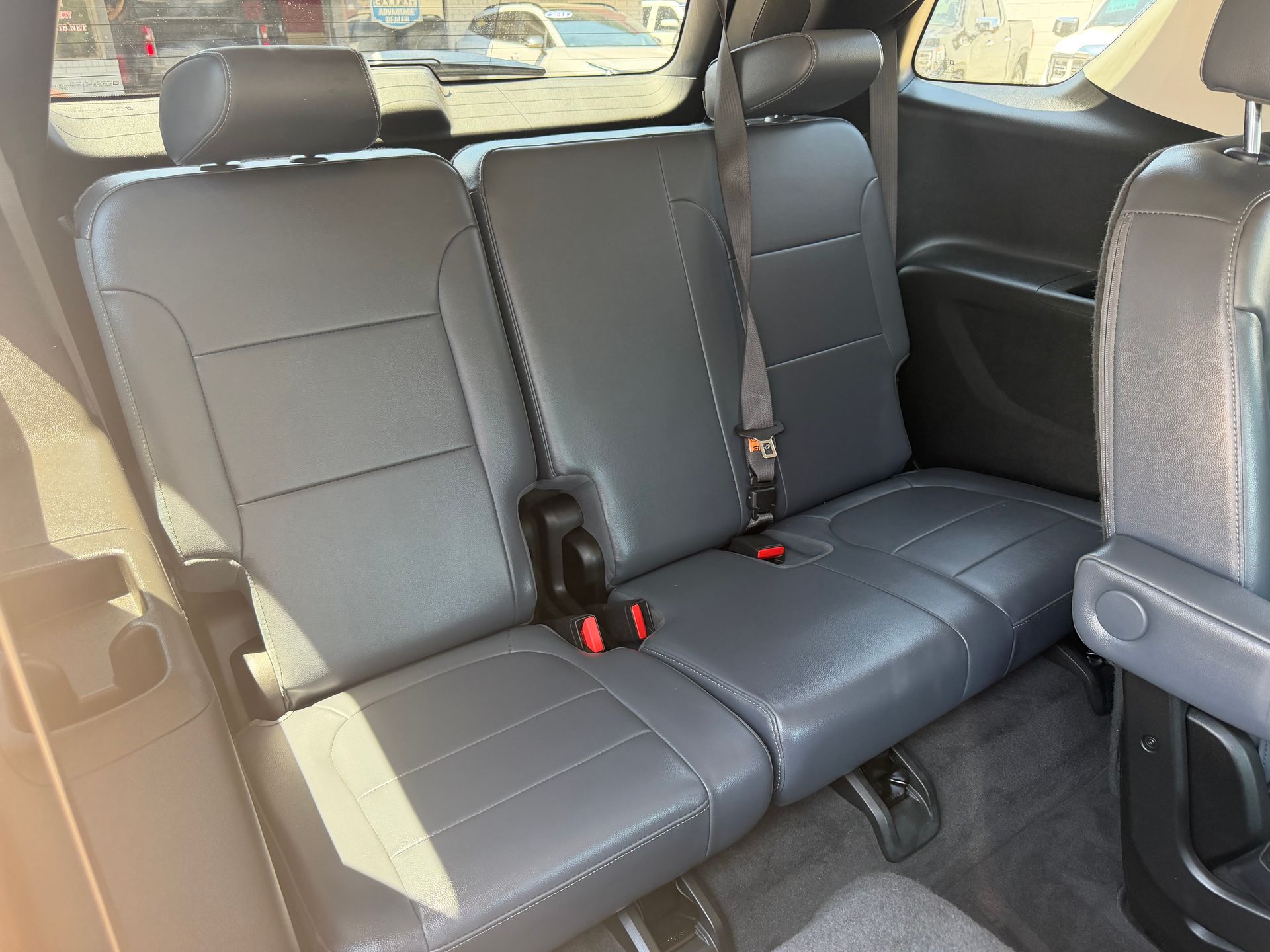 Gray leather back seat in a vehicle interior with three headrests and red seatbelt buckles.