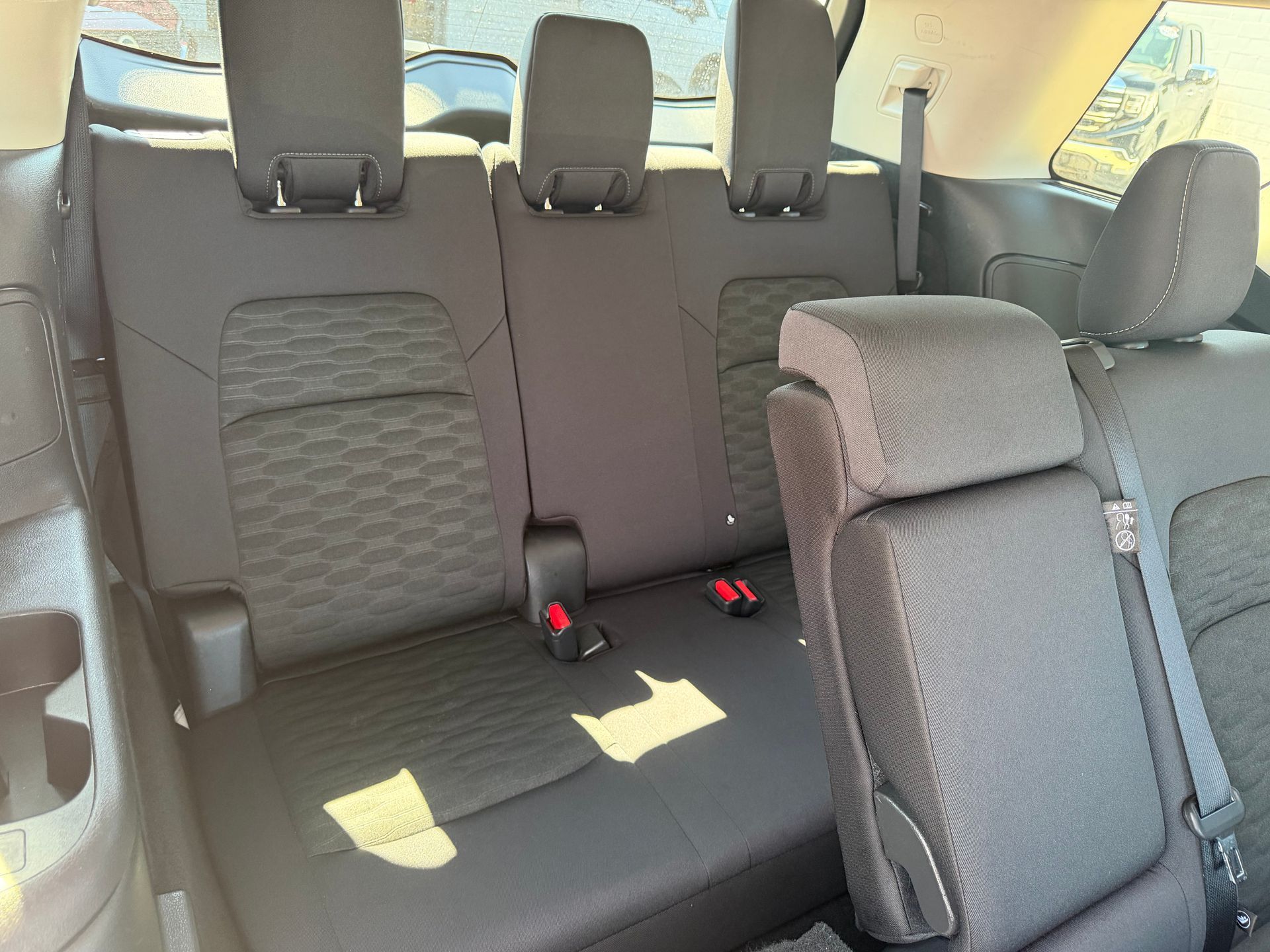 Rear car seat with black upholstery and folded center armrest, viewed from the back
