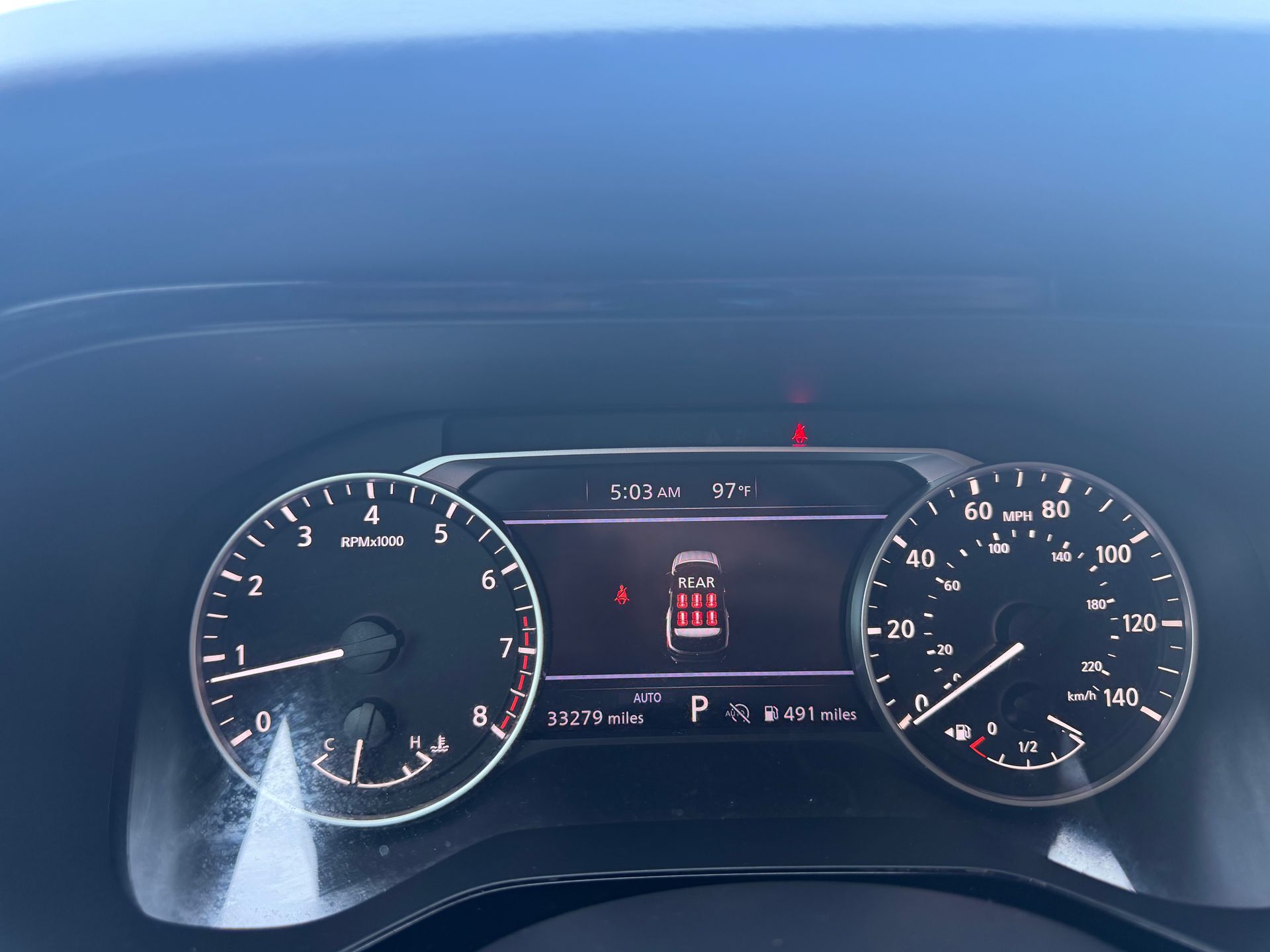 Car dashboard with two analog gauges and a central digital display showing speed and gear.