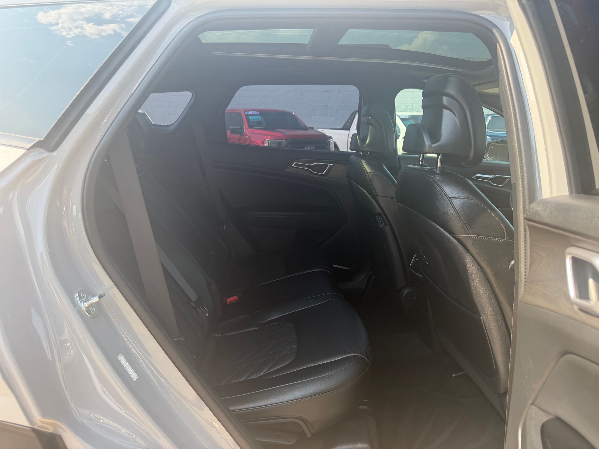 Open car rear door showing black leather back seat and beige interior, with a red car visible outside.